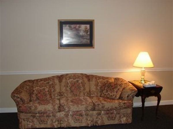 Sofa with floral pattern, small table with lamp, and picture on the wall. Beige walls, black floor.