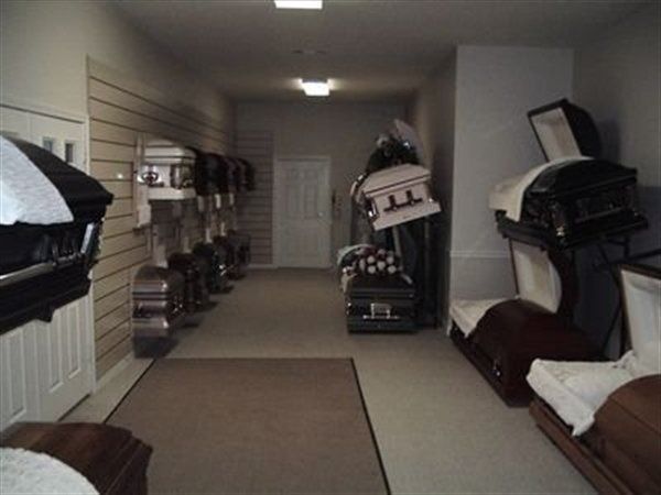 Hallway displaying various open and closed caskets, likely in a funeral home.
