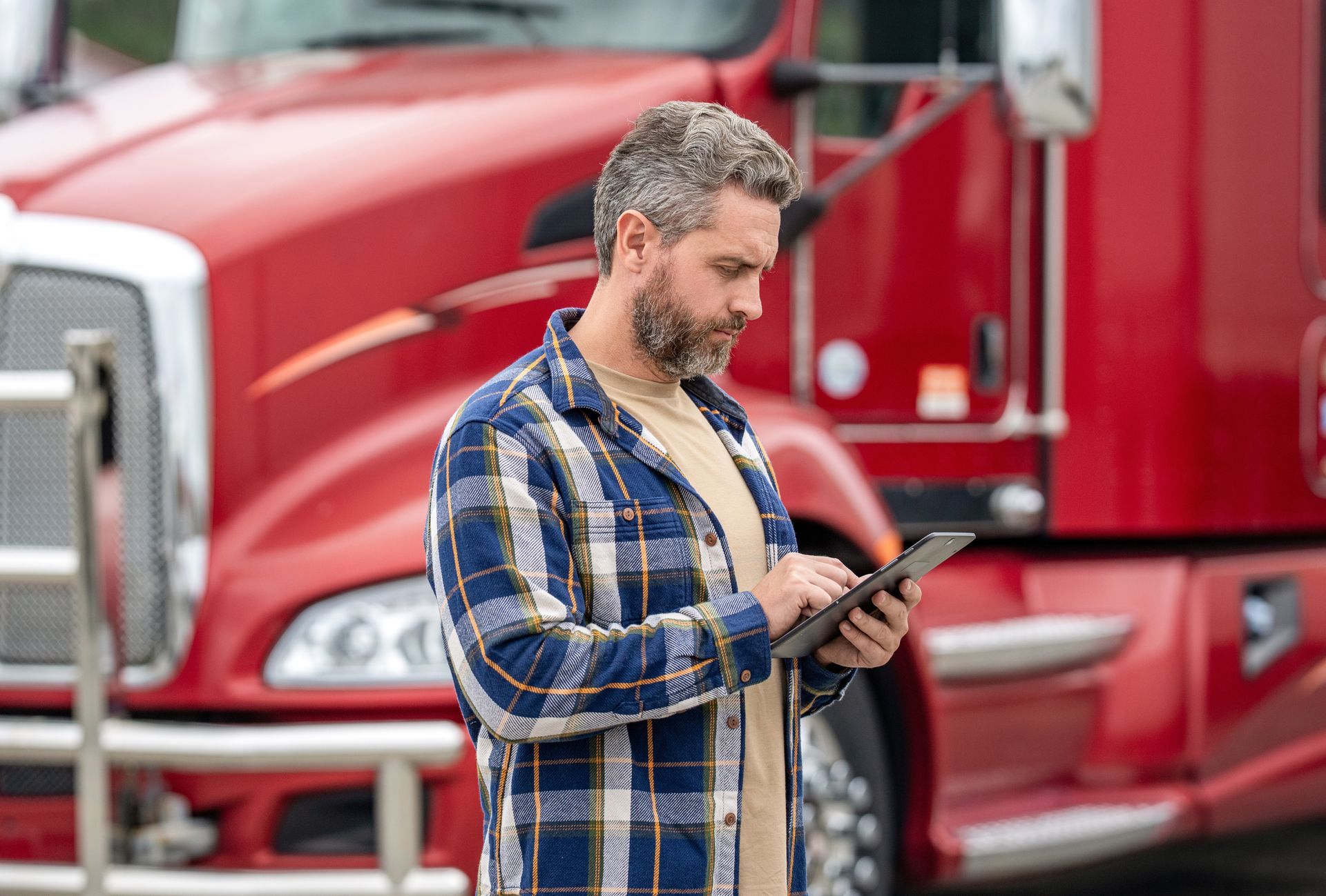 A person in a plaid shirt stands in front of a red semi-truck.