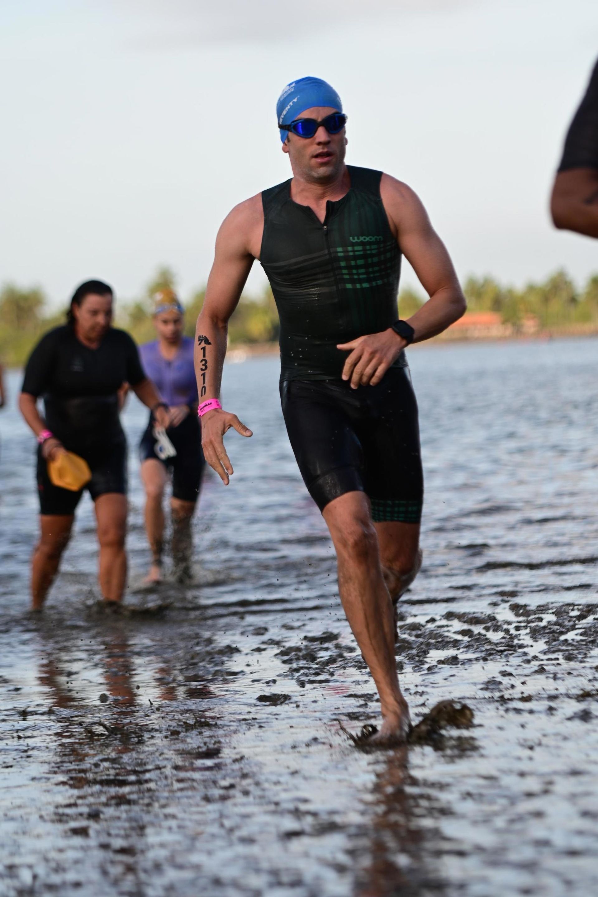 Triatleta ficando sem água, vestindo roupa de neoprene, touca de natação e óculos de sol.