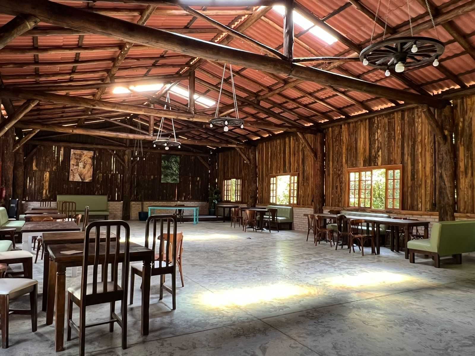 Interior rústico de madeira com mesas, cadeiras e bancos. A luz entra pelas janelas.