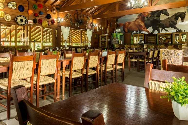 Interior de restaurante em madeira com mesas, cadeiras e pintura de um cavalo. Chapéus enfeitam a parede.