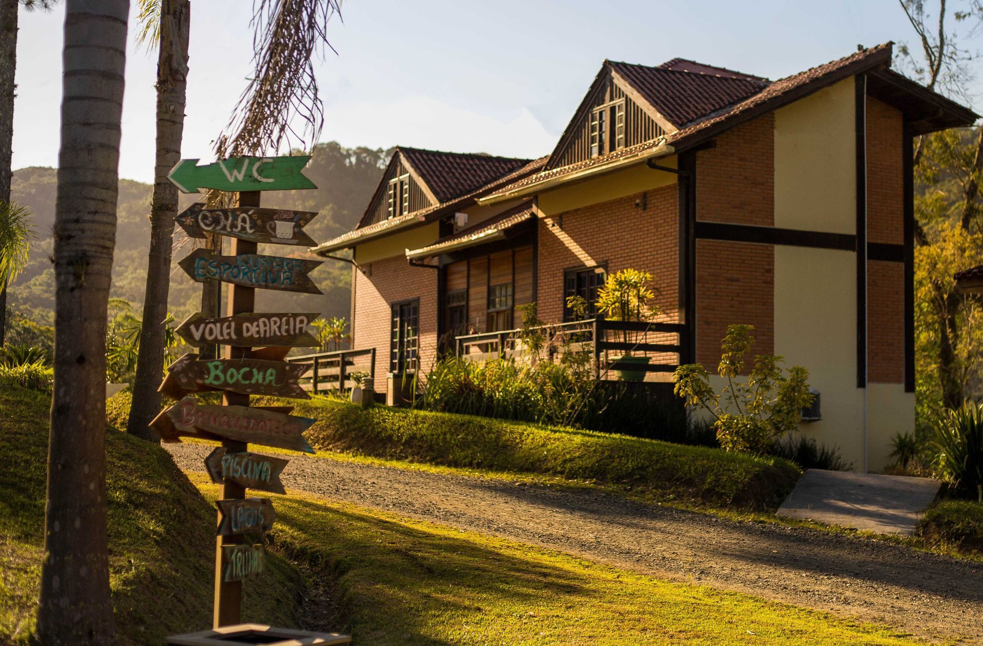 Placa de madeira perto de um prédio de tijolos. A placa indica a localização de um banheiro, uma área de alimentação e outros locais.