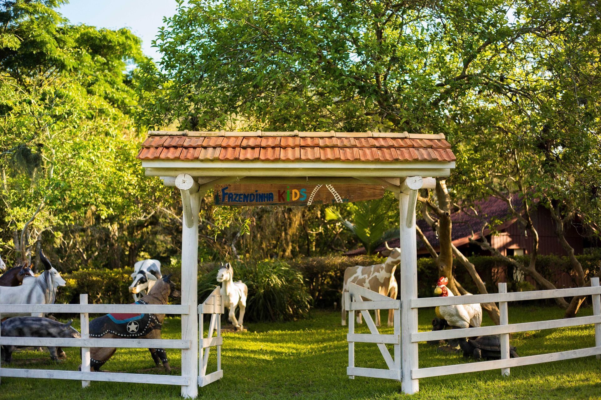 Portão branco que dá acesso a uma área gramada com cavalos e uma placa com a inscrição 