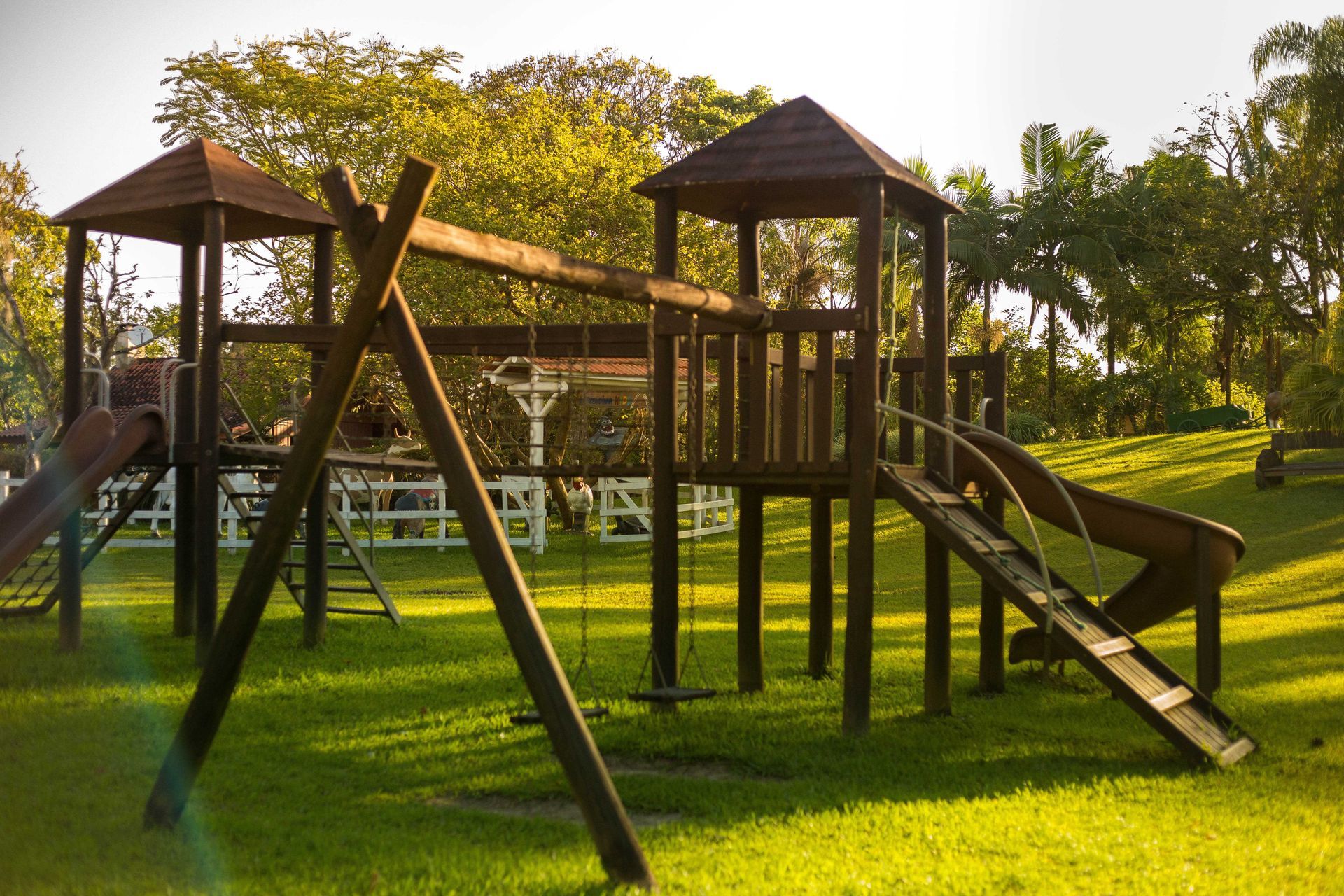 Estrutura de madeira para parque infantil com escorregadores e balanços em um gramado.