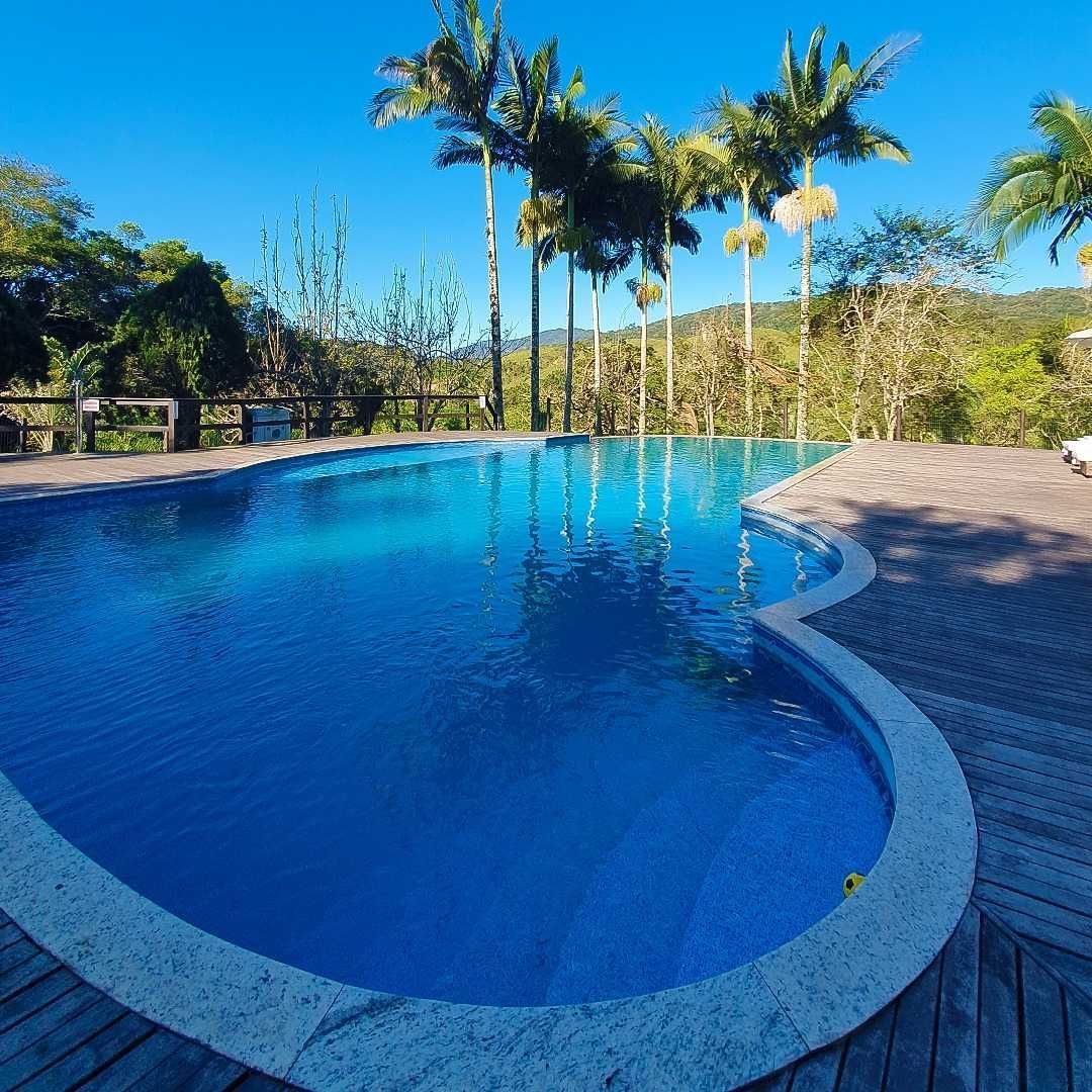 Piscina com água azul, palmeiras e céu claro em um ambiente tropical.