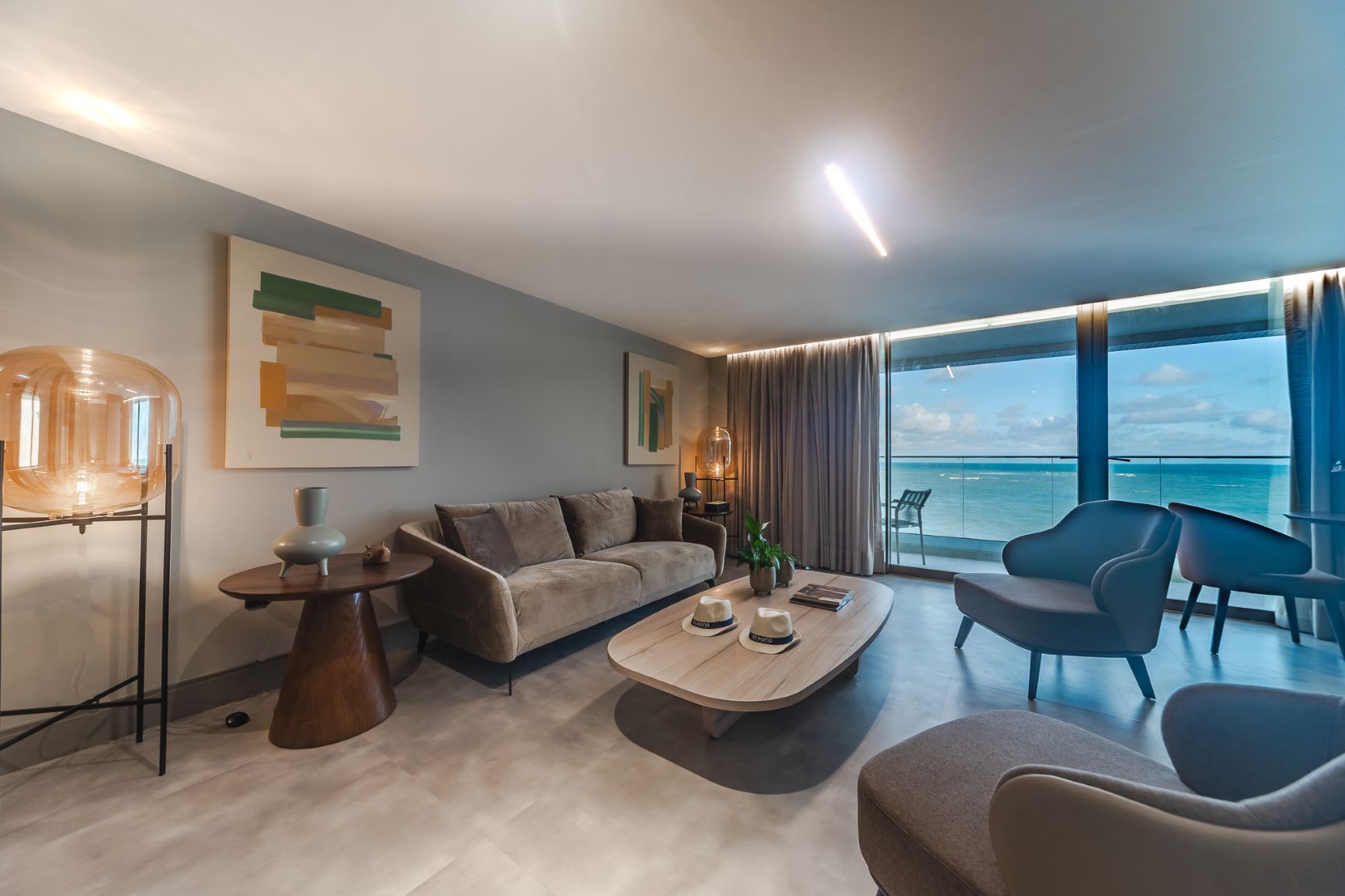 Uma sala de estar com um sofá, cadeiras, uma mesa de centro e uma varanda com vista para o oceano.