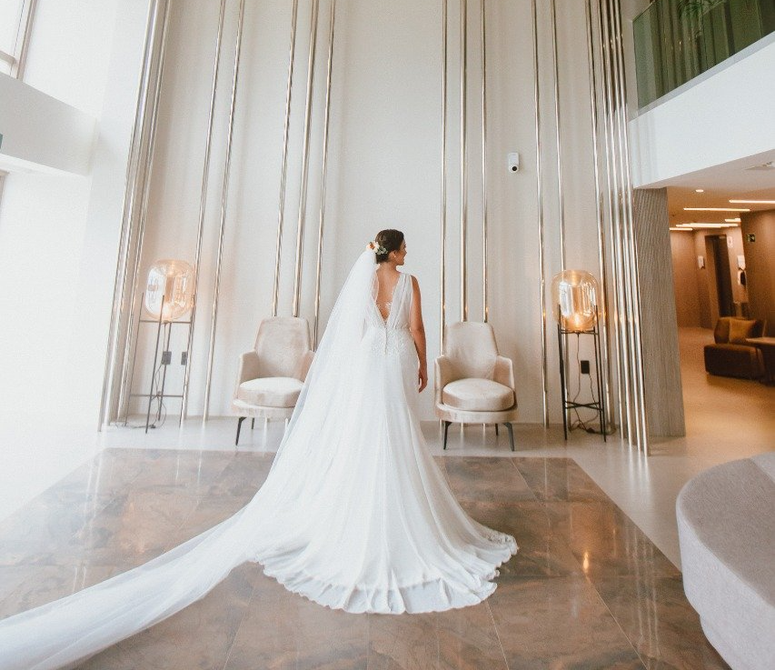 Uma noiva com um longo vestido branco e véu está parada em uma sala.