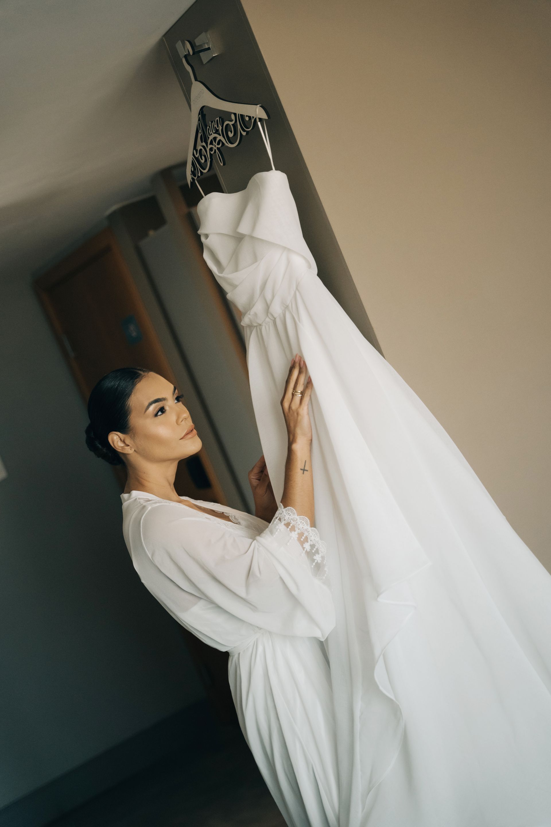 Uma mulher de vestido branco está segurando um vestido de noiva pendurado na parede.