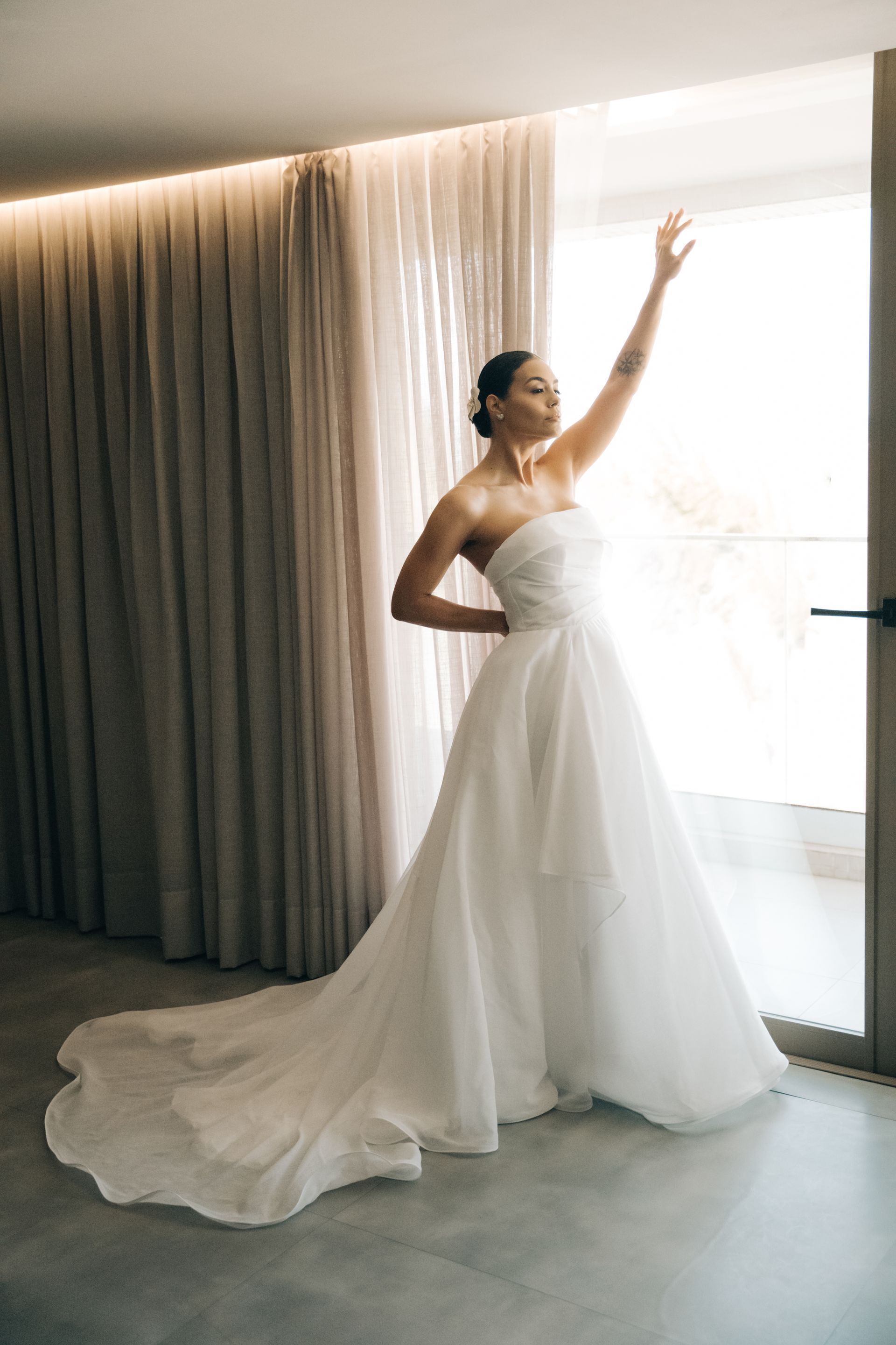 Uma mulher vestida de noiva está parada em frente a uma janela.