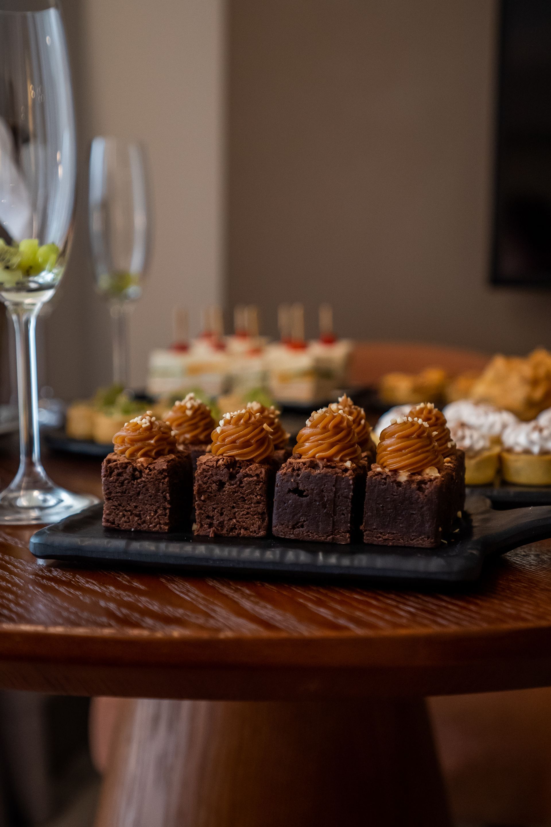 Uma mesa de madeira coberta com uma bandeja de brownies e uma taça de vinho.