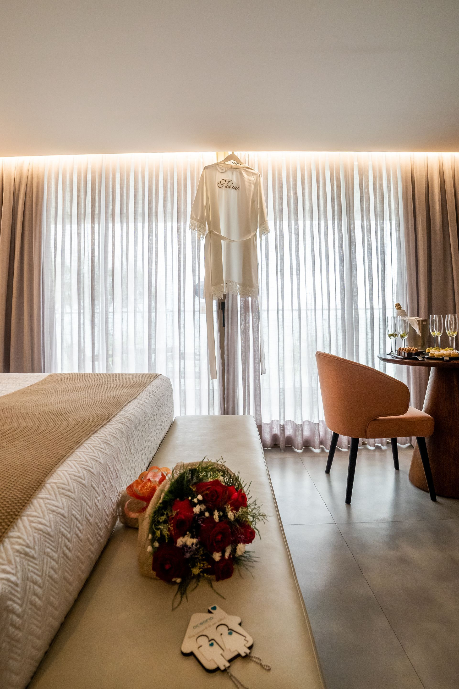 Um buquê de flores está em um banco em um quarto de hotel ao lado de uma cama.