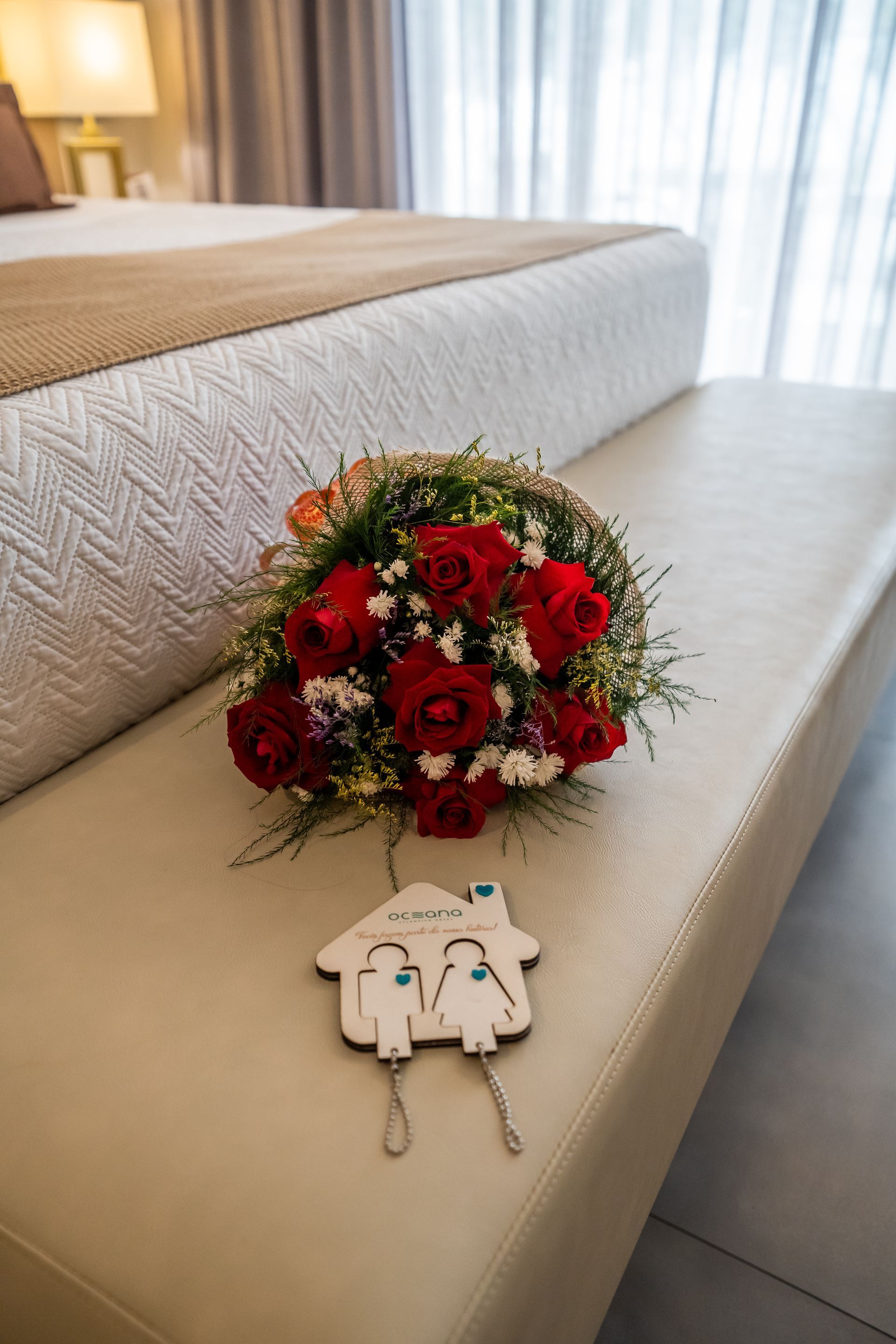 Um buquê de rosas vermelhas está em um banco ao lado de uma cama.