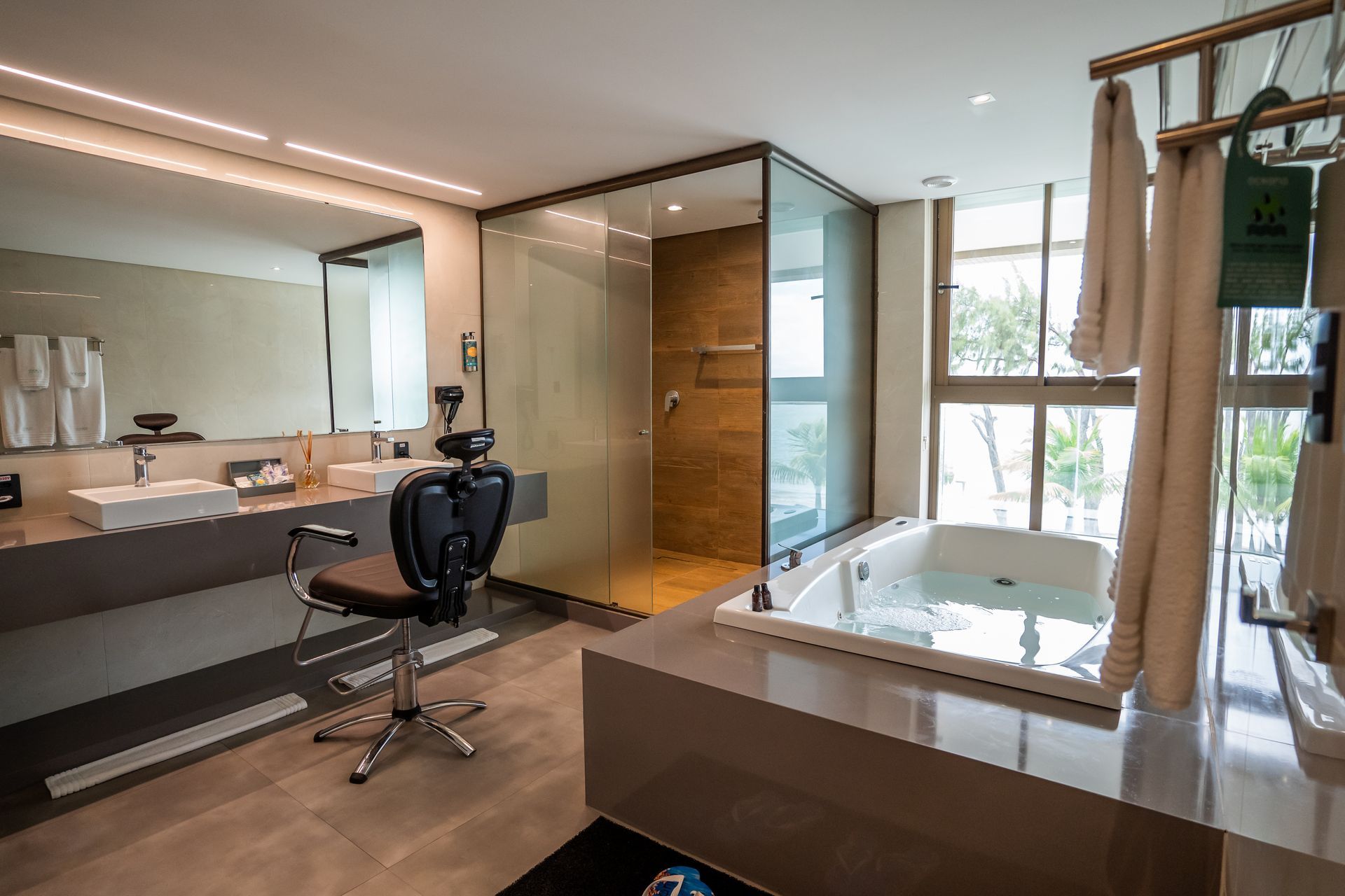 Um banheiro com banheira de hidromassagem, pia, espelho e cadeira.