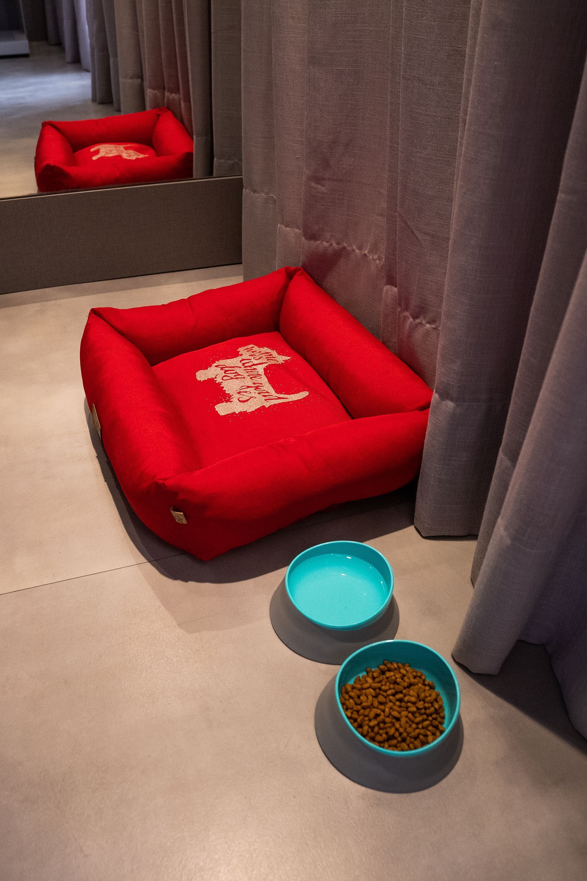 Uma cama vermelha para cachorro está ao lado de duas tigelas de comida para cachorro.