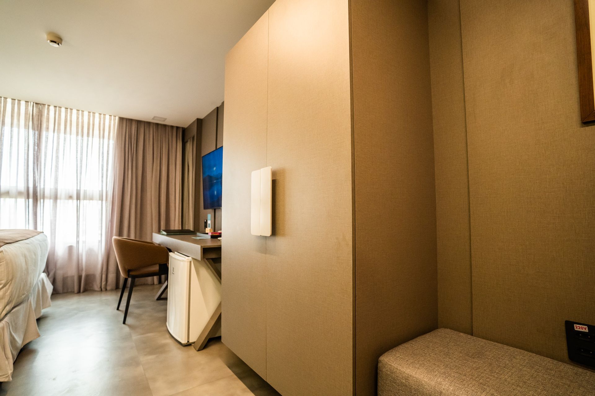 Um quarto de hotel com uma cama, escrivaninha, cadeira e televisão.