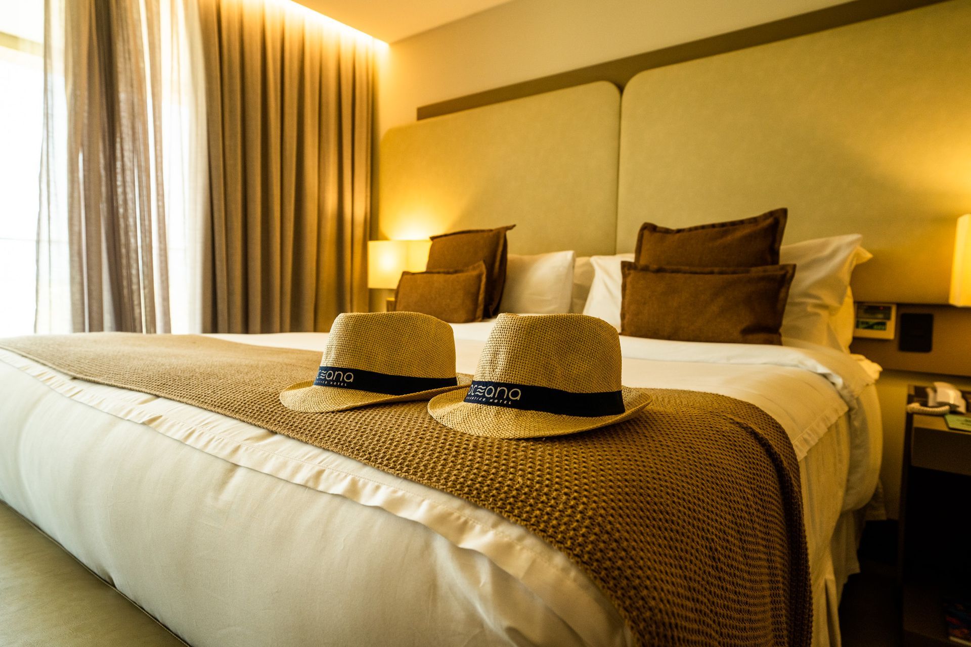 Dois chapéus estão sobre uma cama em um quarto de hotel.