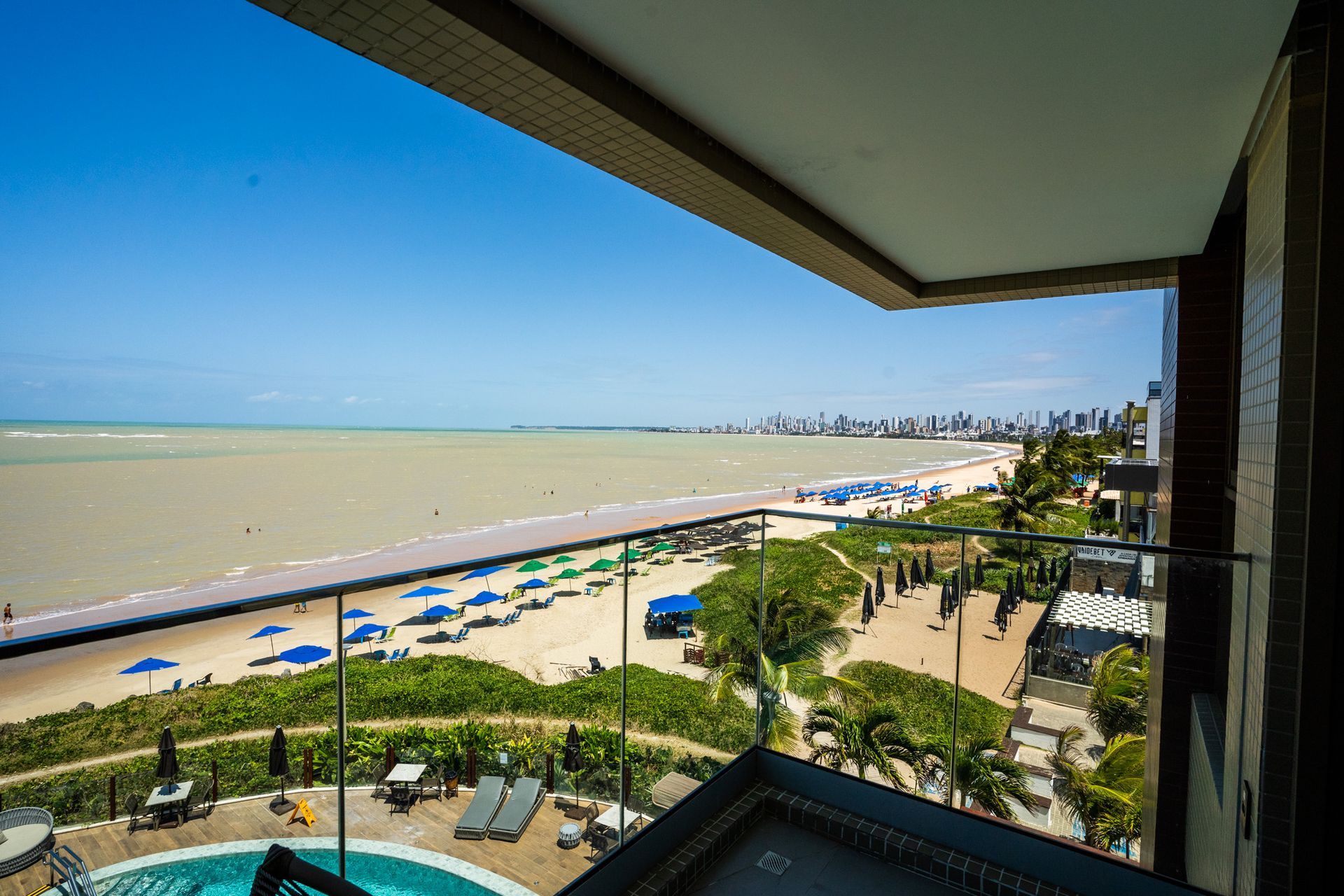 Vista de uma praia e de uma piscina a partir de uma varanda.