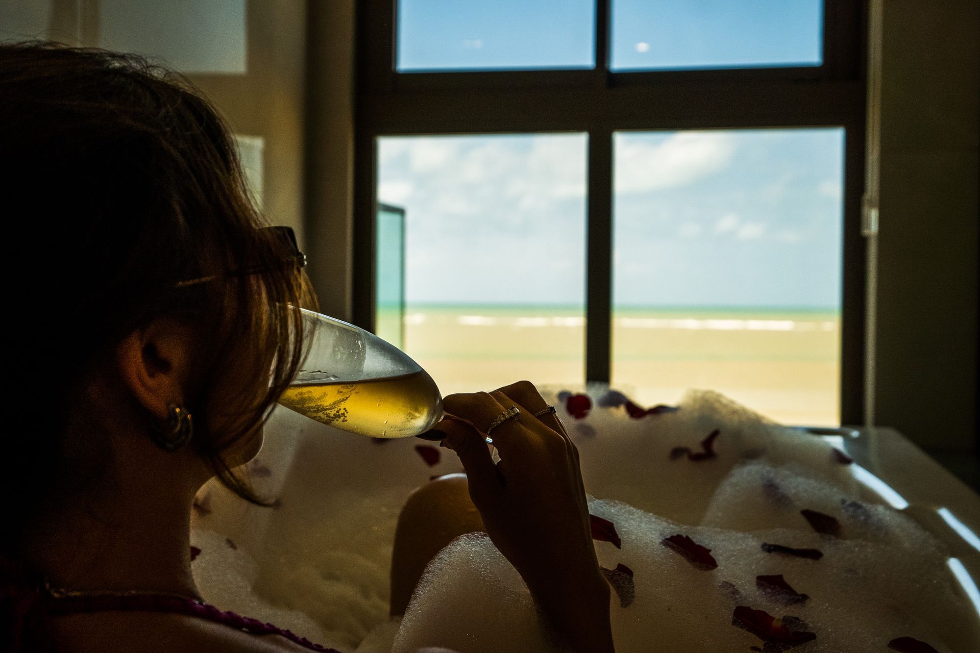 Uma mulher está sentada em uma banheira bebendo uma taça de vinho.