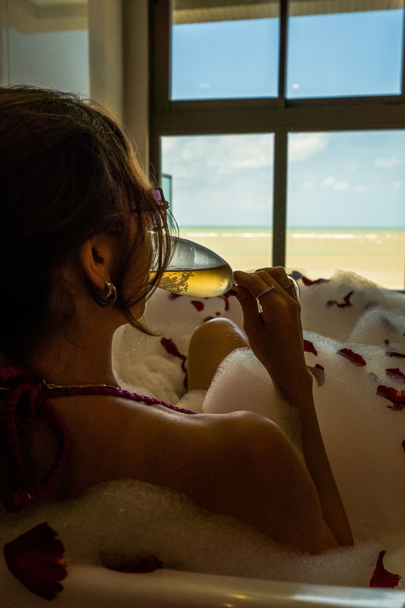 Uma mulher está tomando banho com uma taça de vinho.