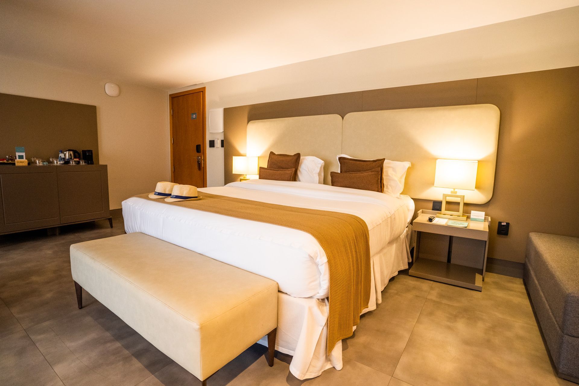 Um quarto de hotel com uma cama grande e um banco.