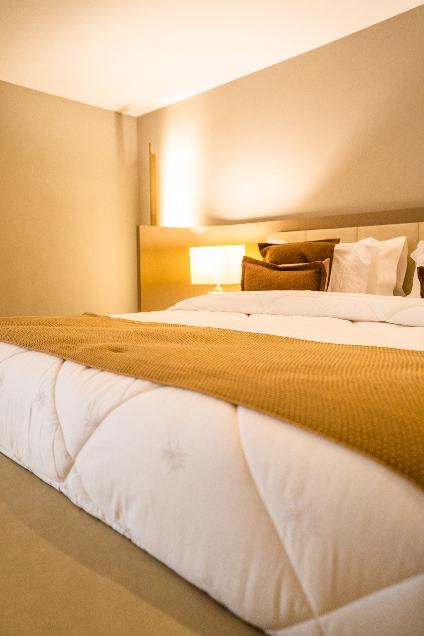 Uma cama com um edredom branco e travesseiros marrons em um quarto de hotel.