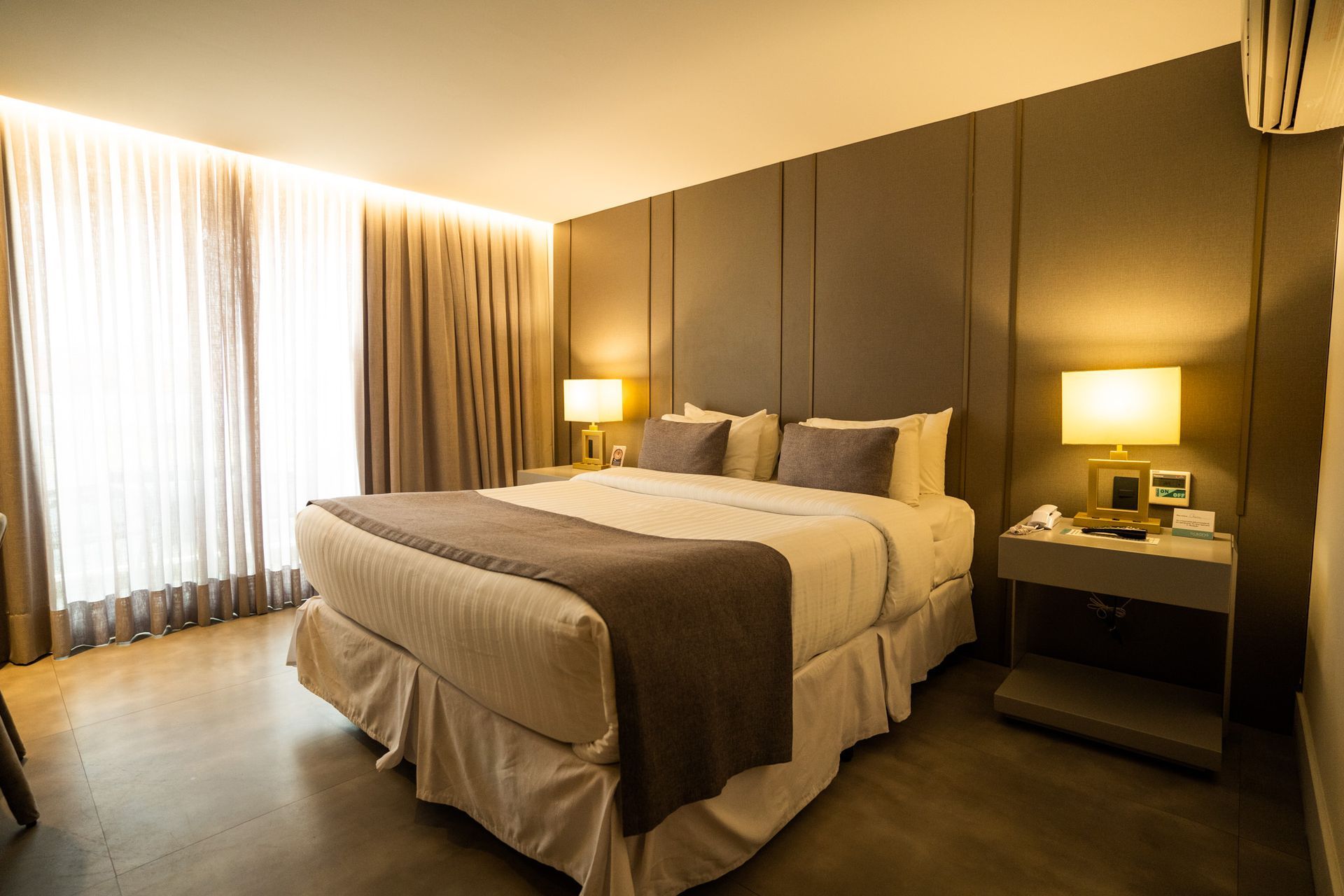 Um quarto de hotel com uma cama king size, lâmpadas e uma janela grande.