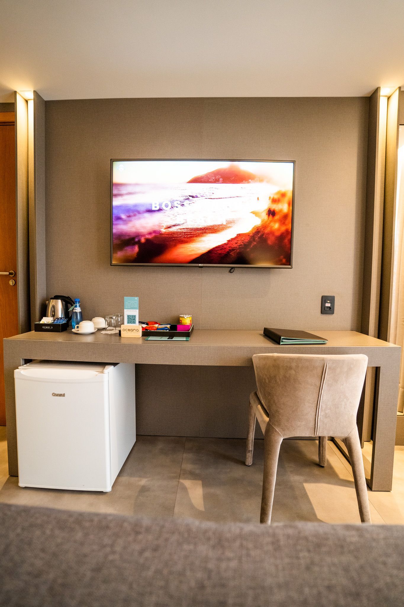 Um quarto de hotel com mesa, cadeira, televisão e geladeira.