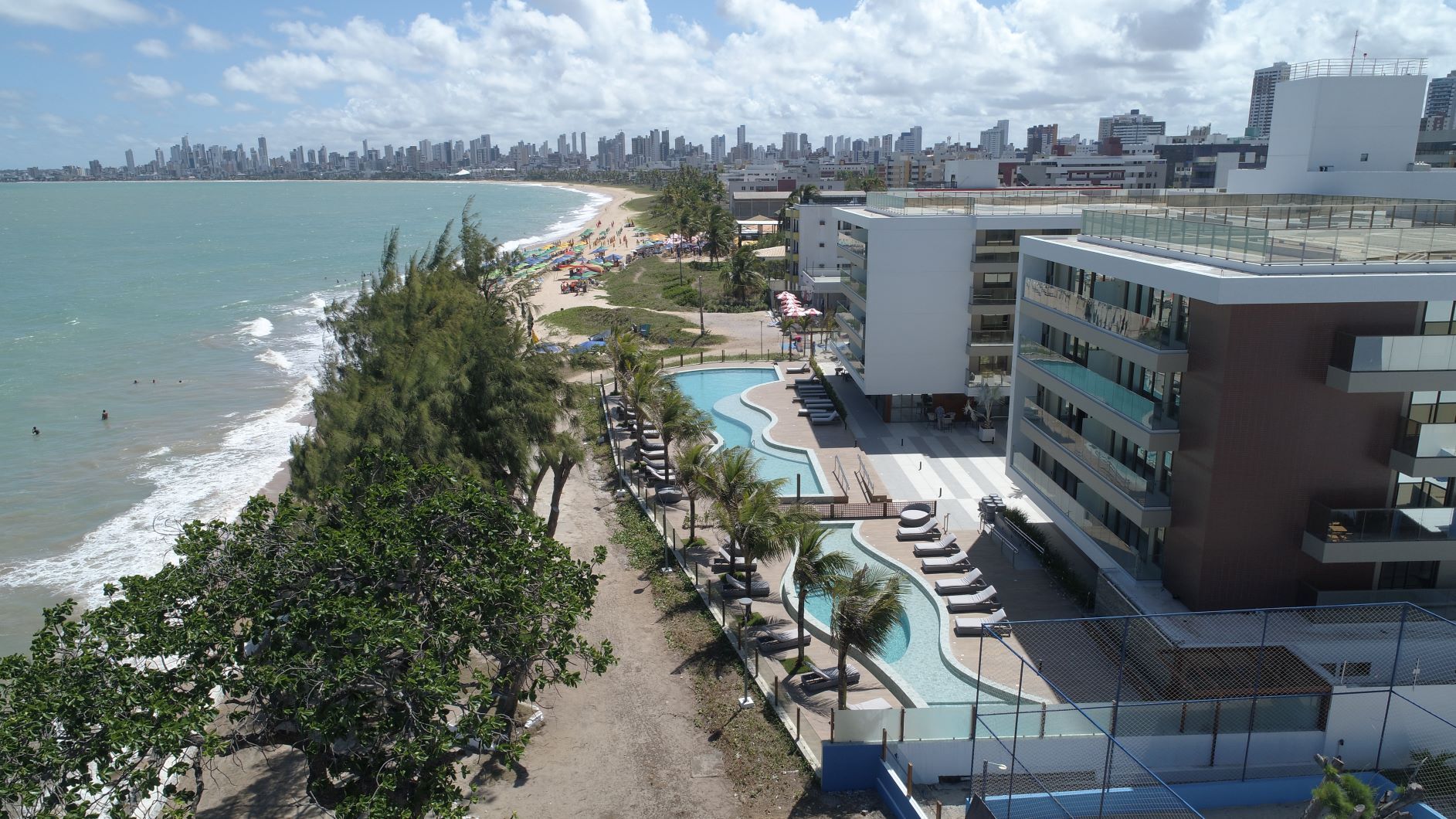 Uma vista aérea de uma praia com um grande edifício em primeiro plano