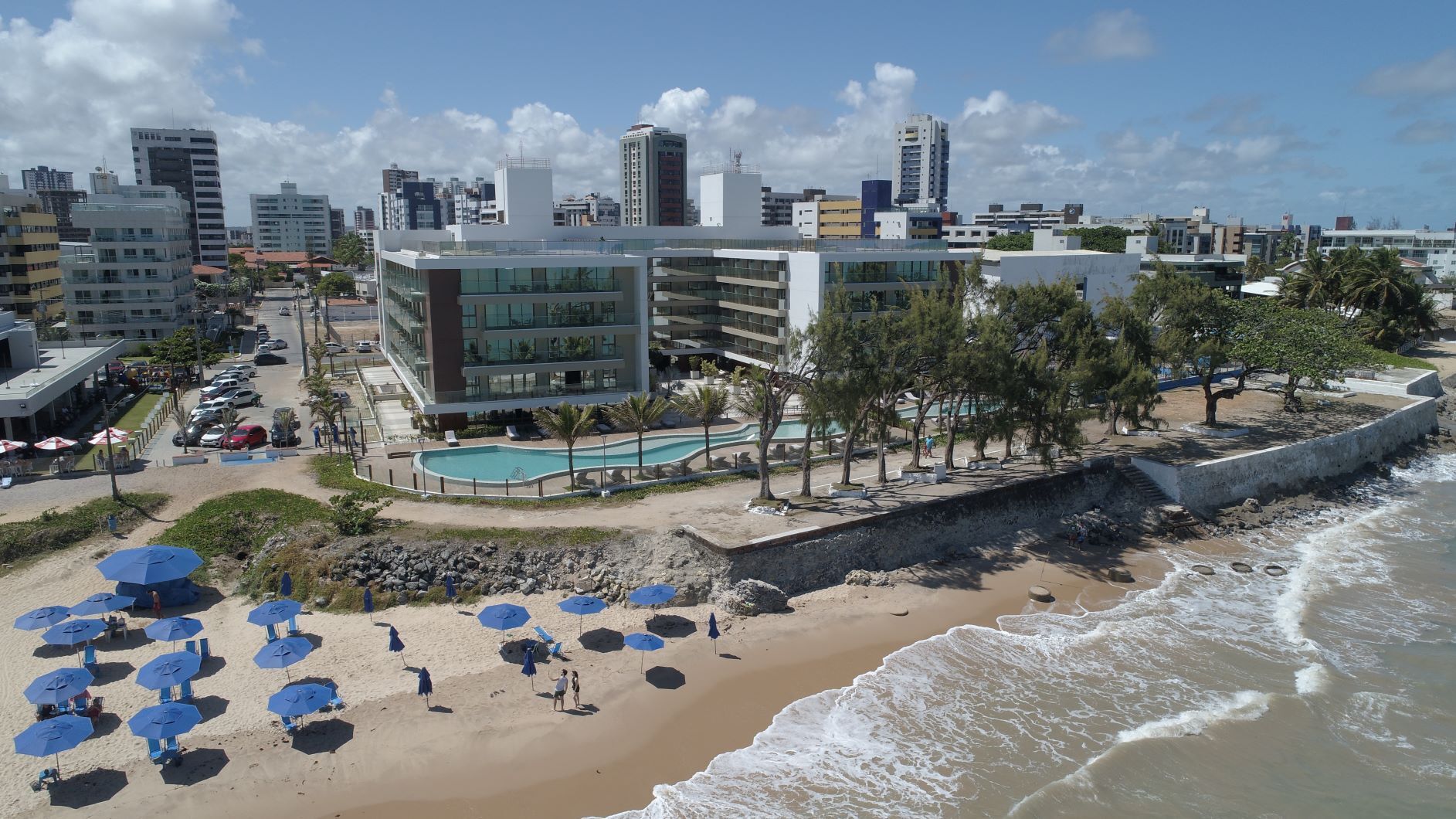 Uma vista aérea de uma praia com guarda-sóis e uma cidade ao fundo.
