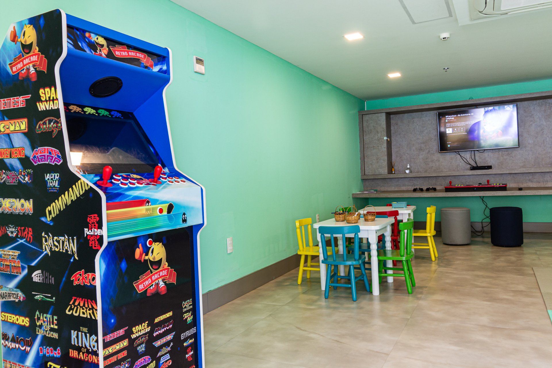 Uma sala com mesas e cadeiras e uma máquina de fliperama.