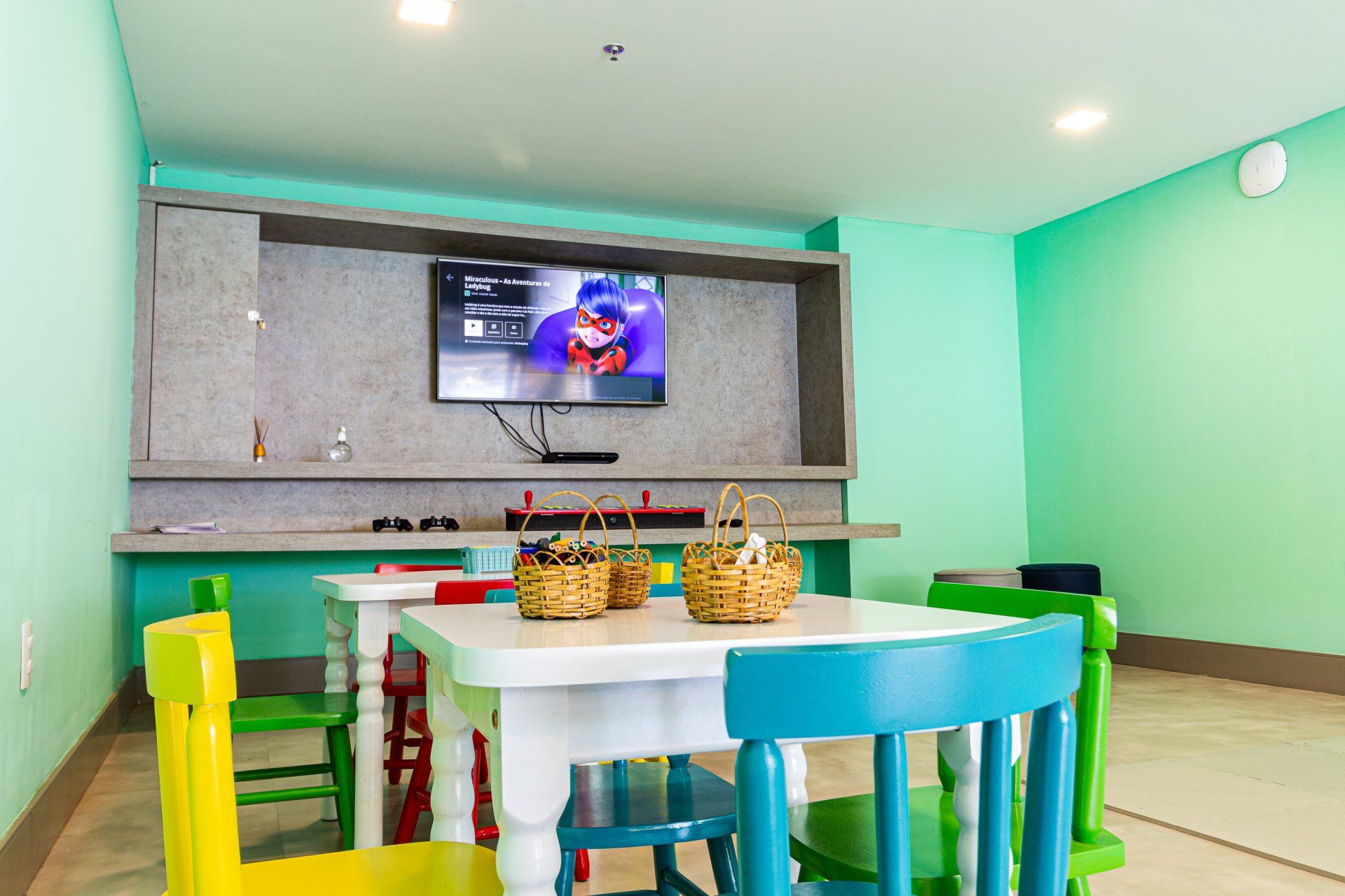 Uma sala para crianças com mesa, cadeiras e televisão.