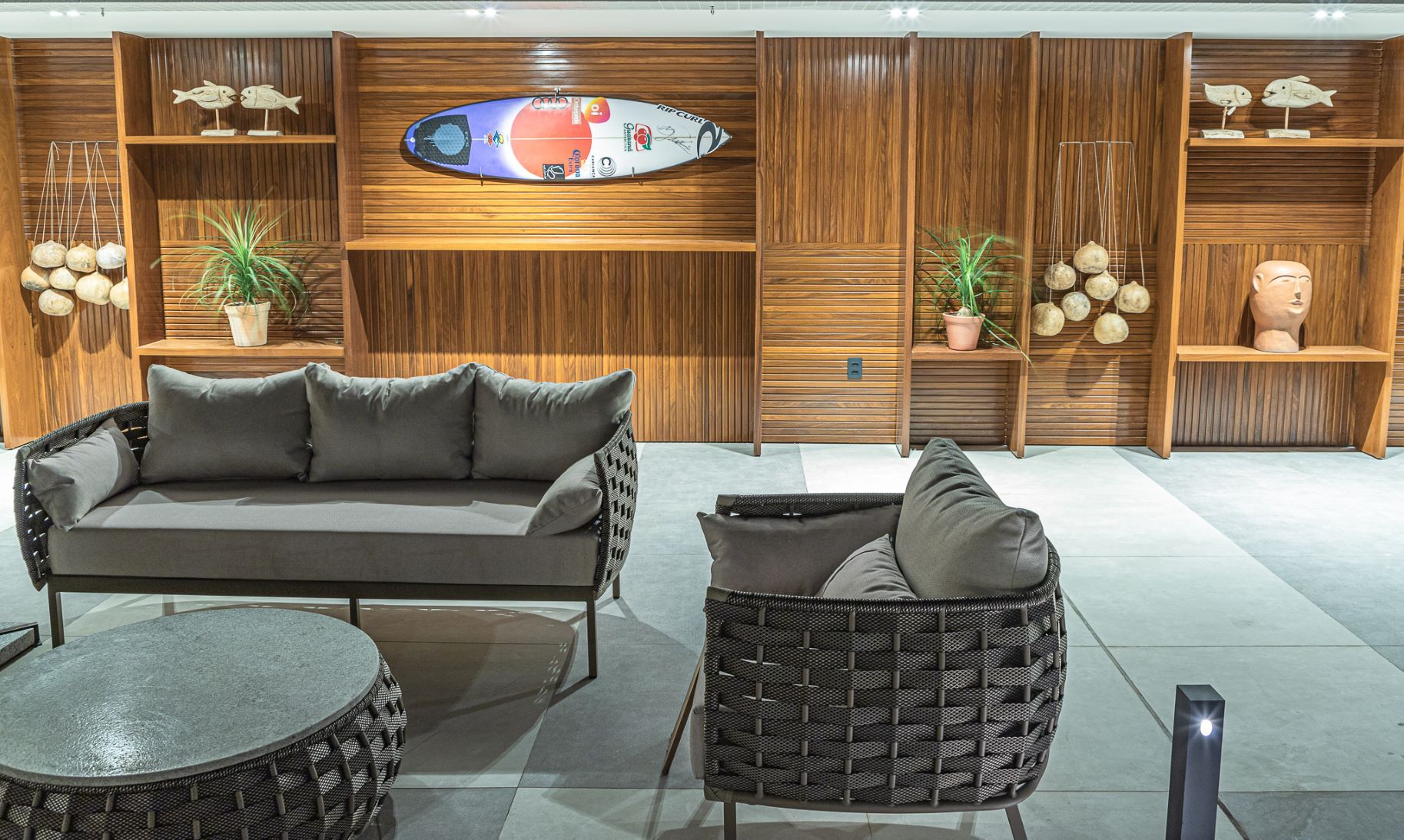 Uma sala de estar com um sofá, cadeira, mesa e prancha de surfe na parede.