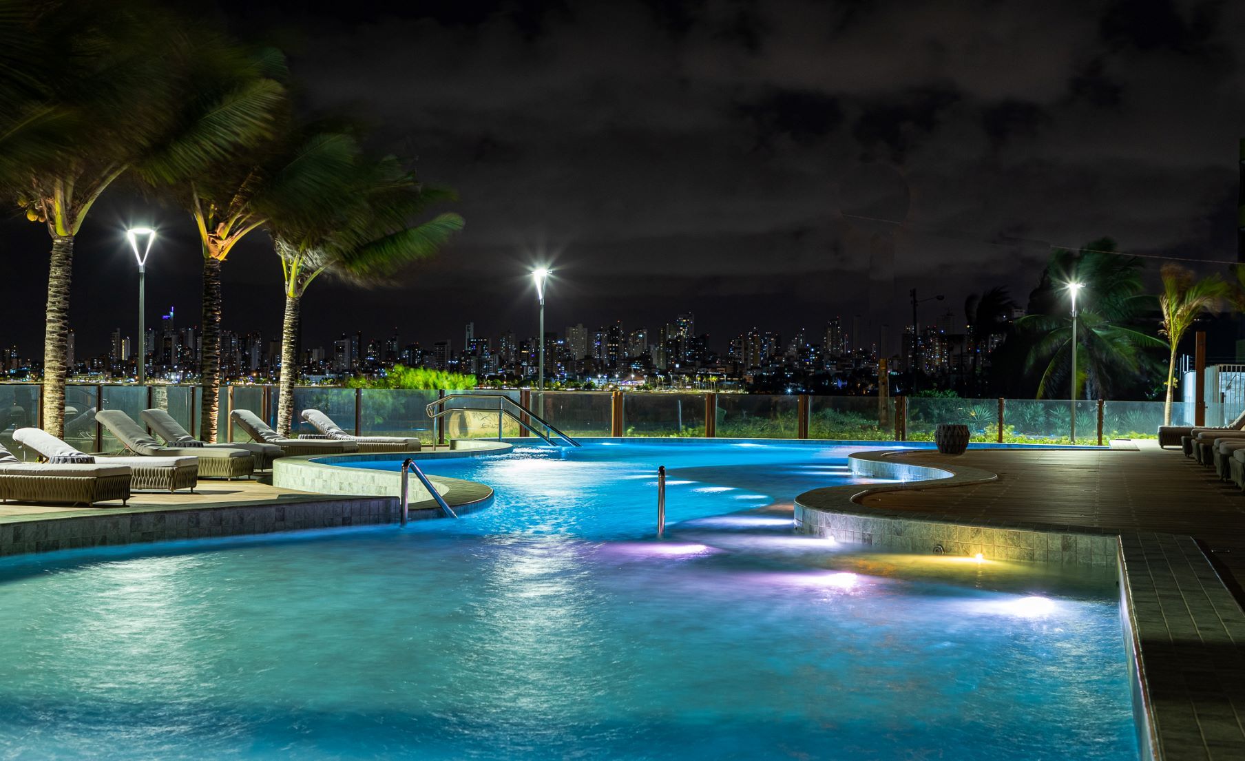 Uma grande piscina iluminada à noite com uma cidade ao fundo.