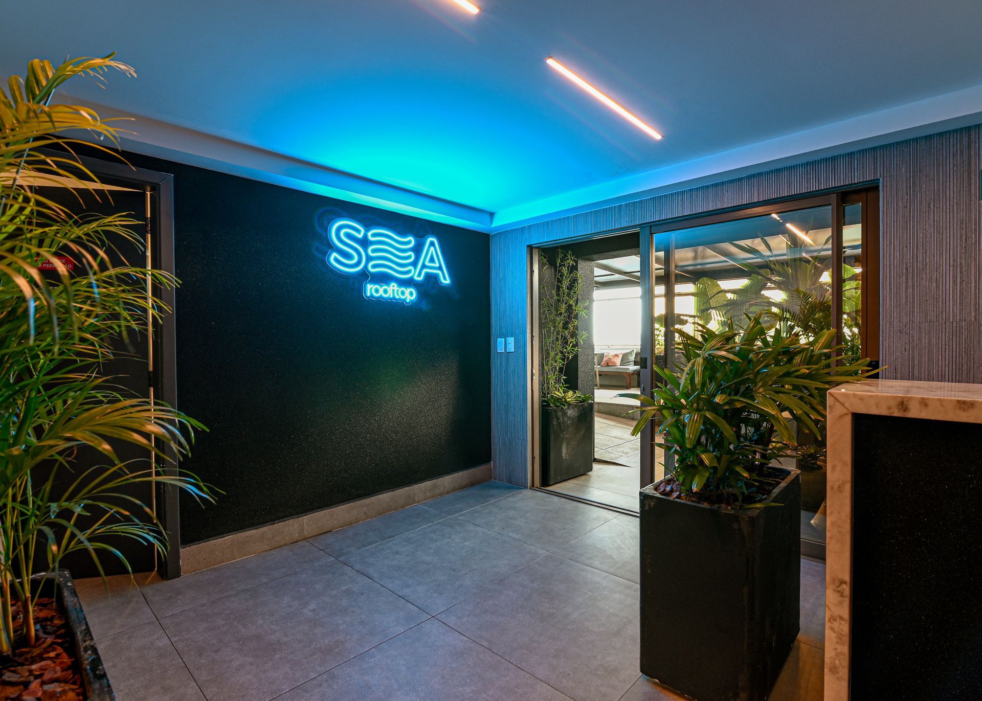 Um corredor com plantas e uma placa de neon que diz