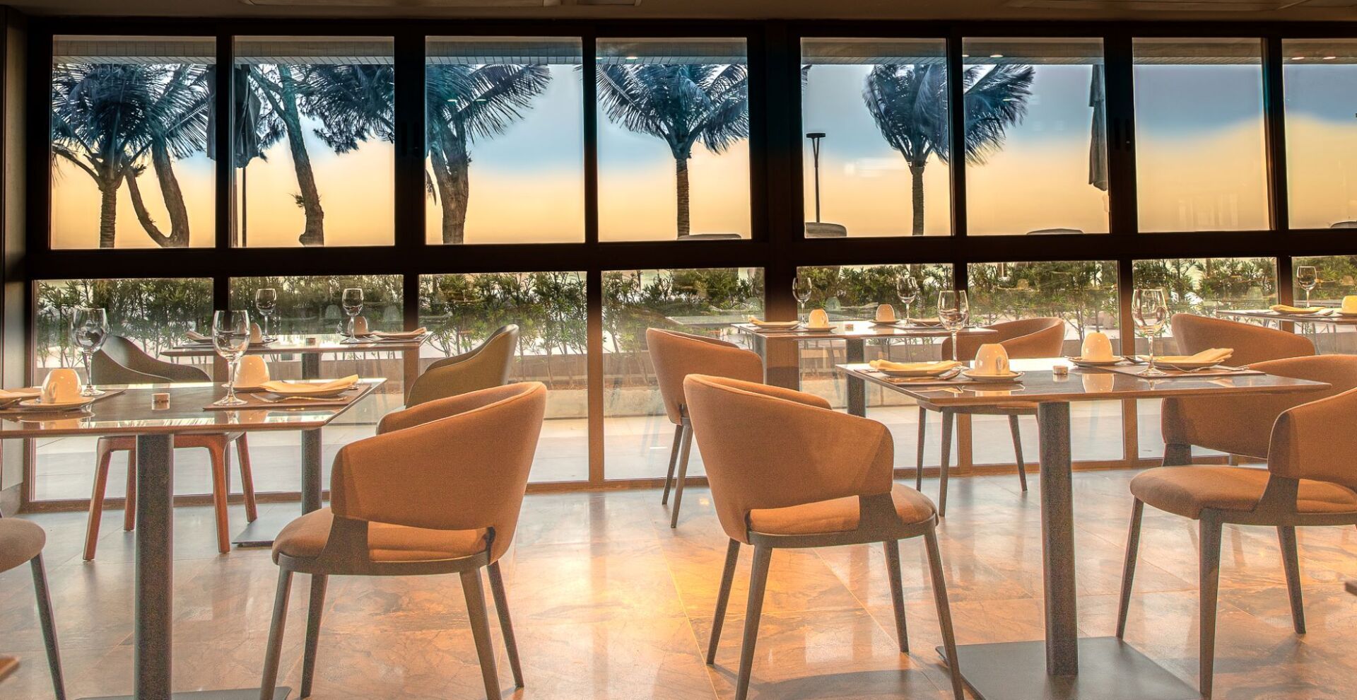 Um restaurante com mesas e cadeiras e vista para as árvores através das janelas.