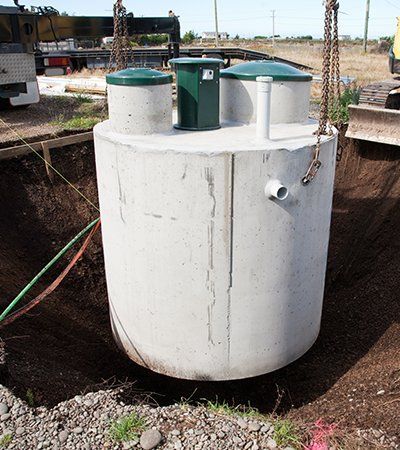 A large cylindrical concrete septic tank being lowered into a hole by chains.