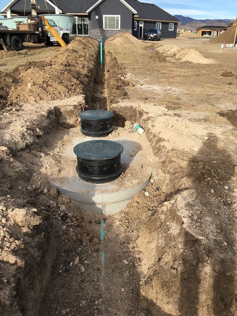 A new septic tank installed in a trench at a residential construction site with pipes connected at both ends.