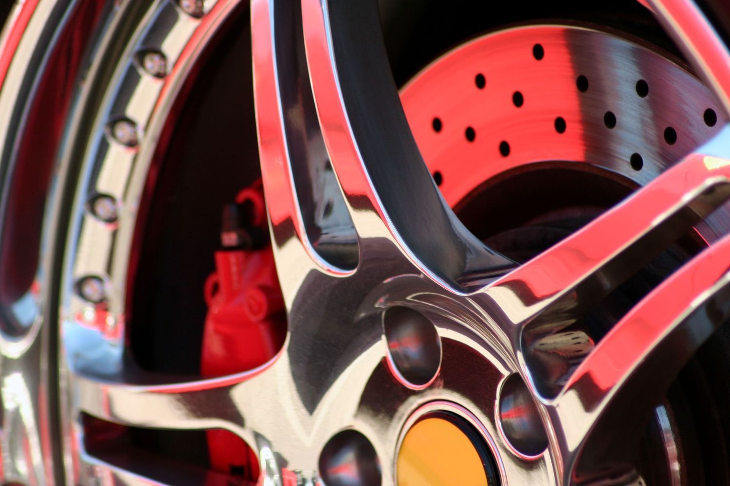 Close-up of a polished chrome car wheel featuring a red brake caliper and a perforated brake disc.