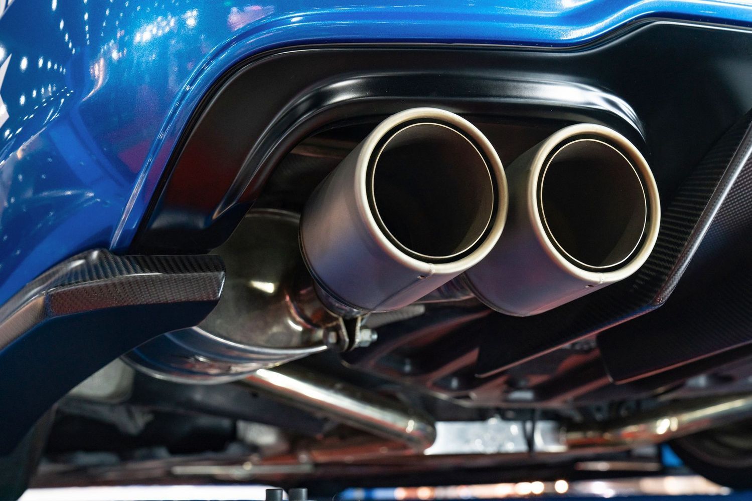 Close-up of the dual exhaust pipes and dark-blue bumper of a sports car from a low-angle perspective.