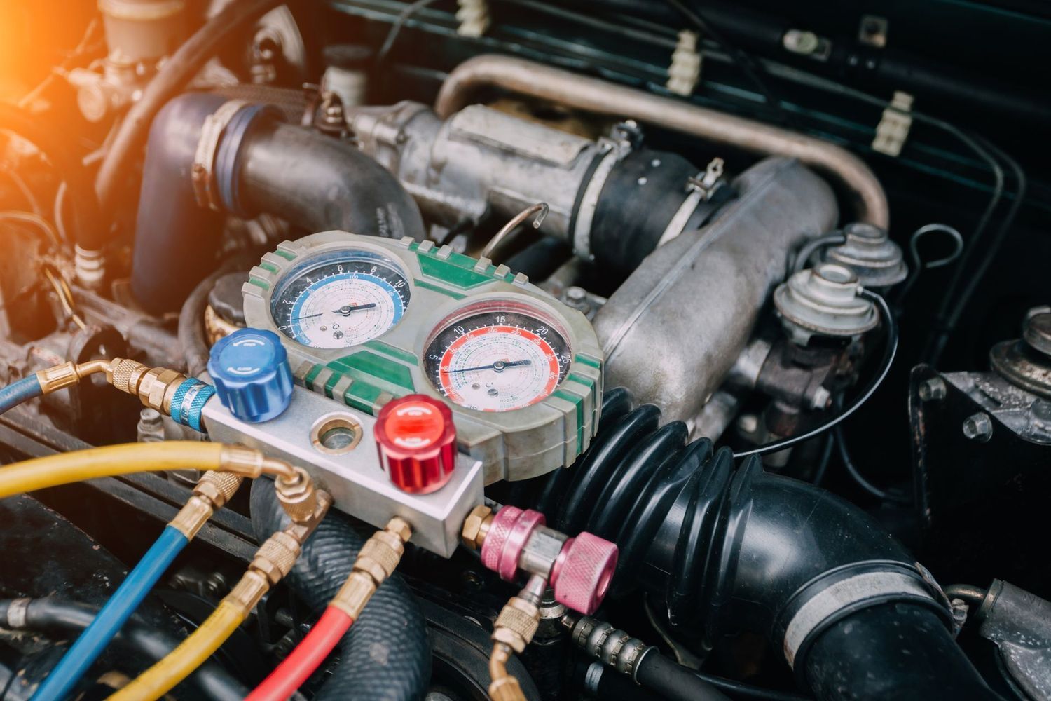 A manifold gauge set with blue, red, and yellow hoses connected to an open car engine to test the air conditioning system.