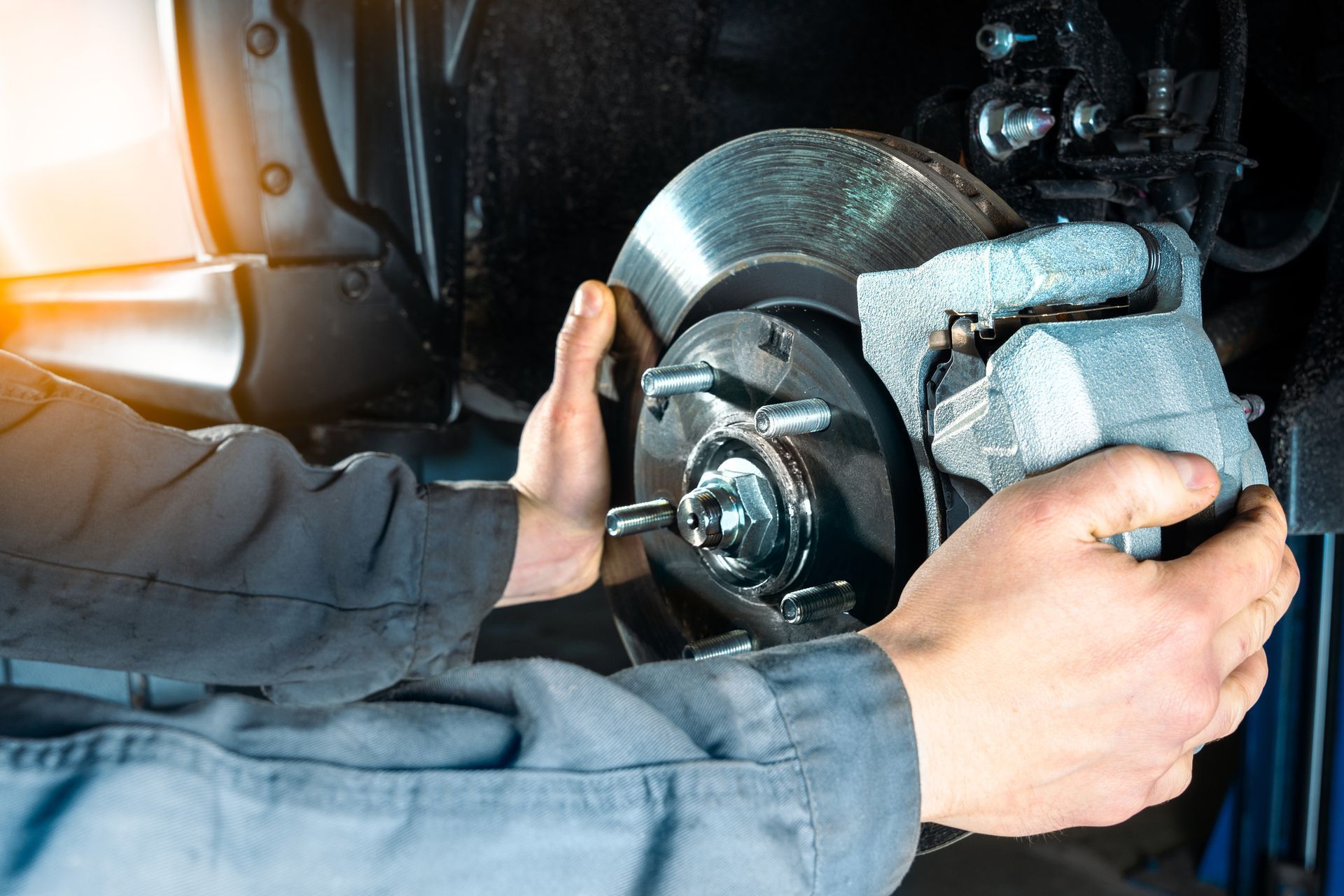 A mechanic's hands installing a brake caliper onto a vehicle's brake rotor.