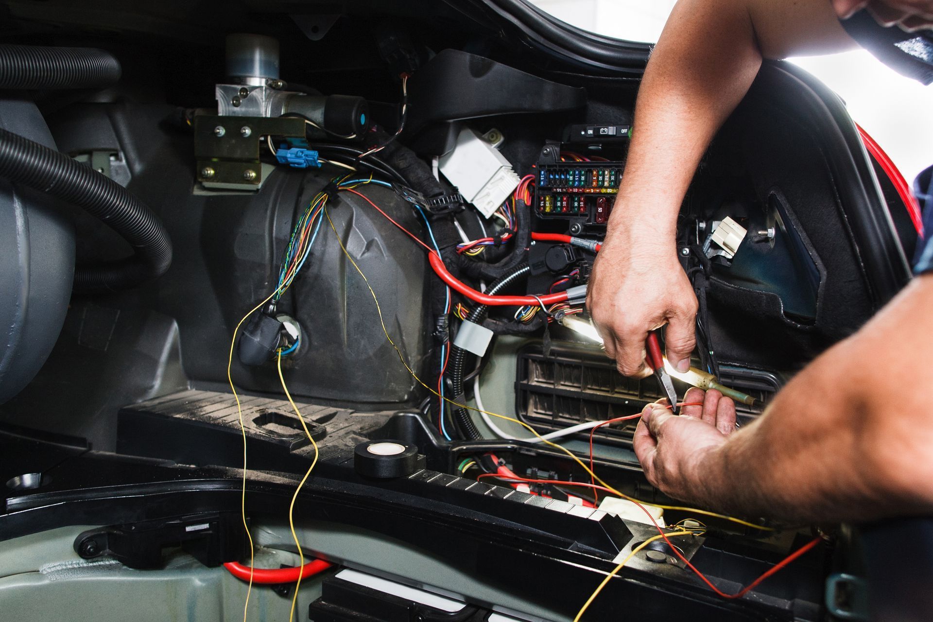 A close-up view of hands working on automotive electrical wiring inside a car trunk.