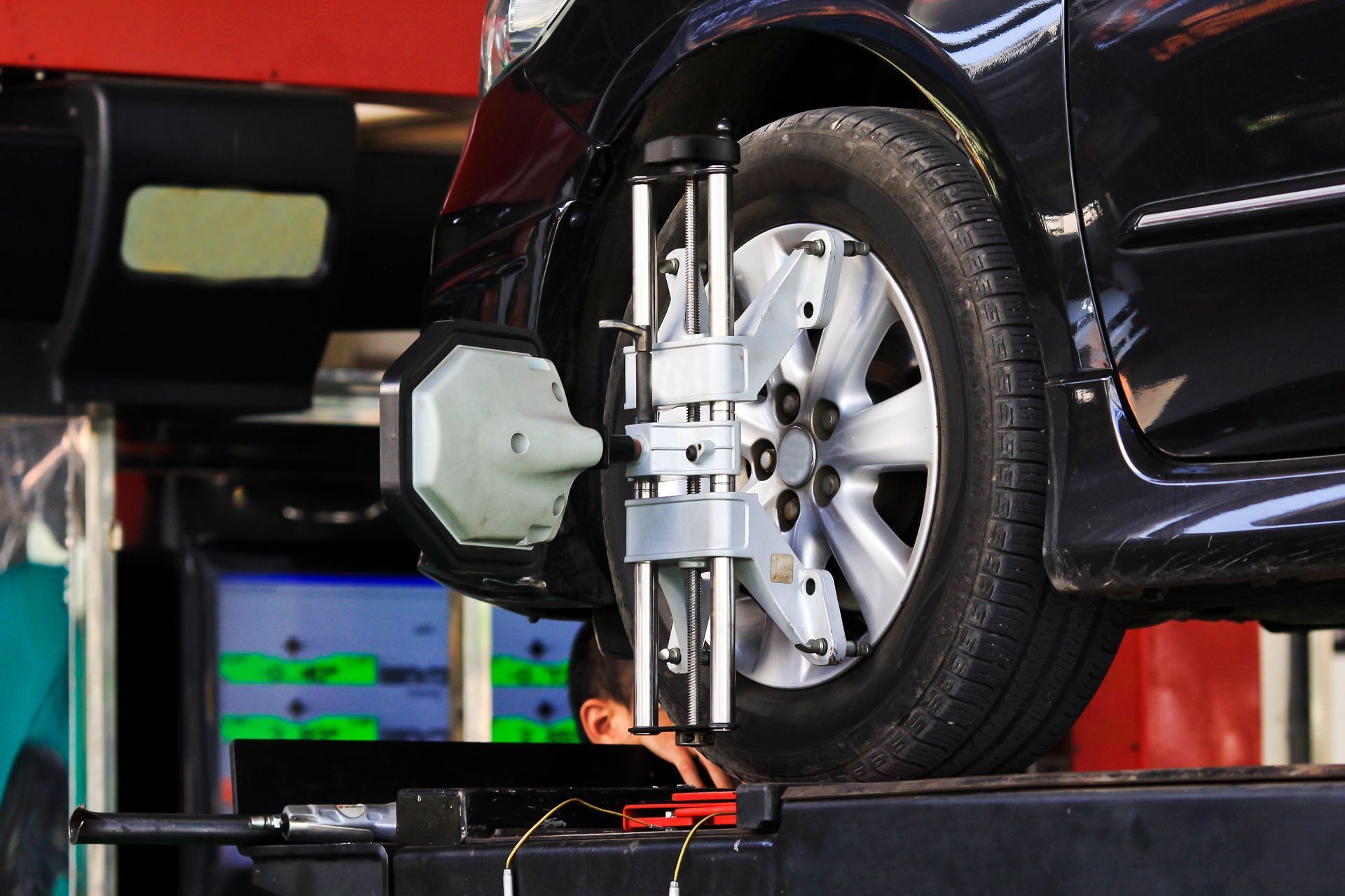 A technician performs a wheel alignment on a black car using specialized diagnostic sensors in a garage setting.