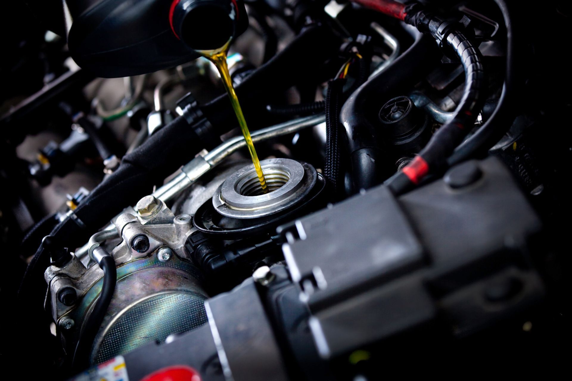 A stream of golden engine oil pouring from a bottle into a car engine's open oil filler neck.