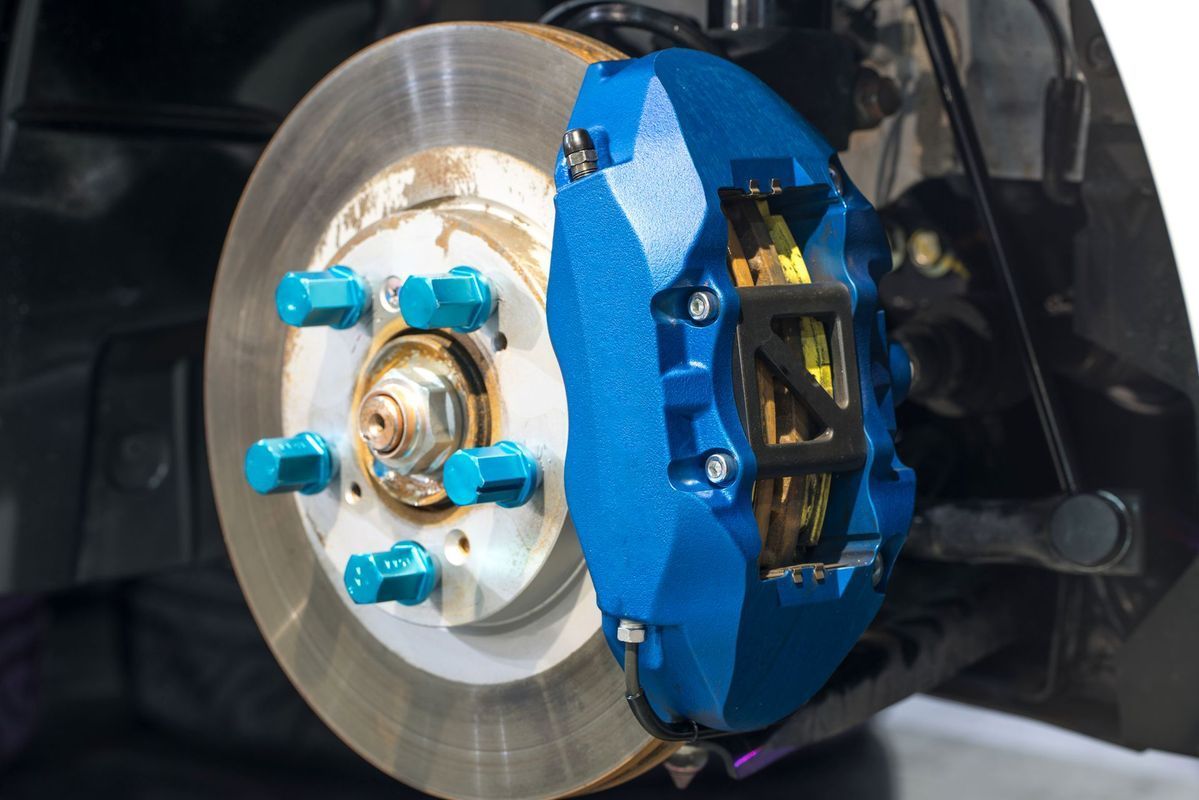 A close-up of a bright blue performance brake caliper mounted on a car’s brake disc with teal lug nuts.