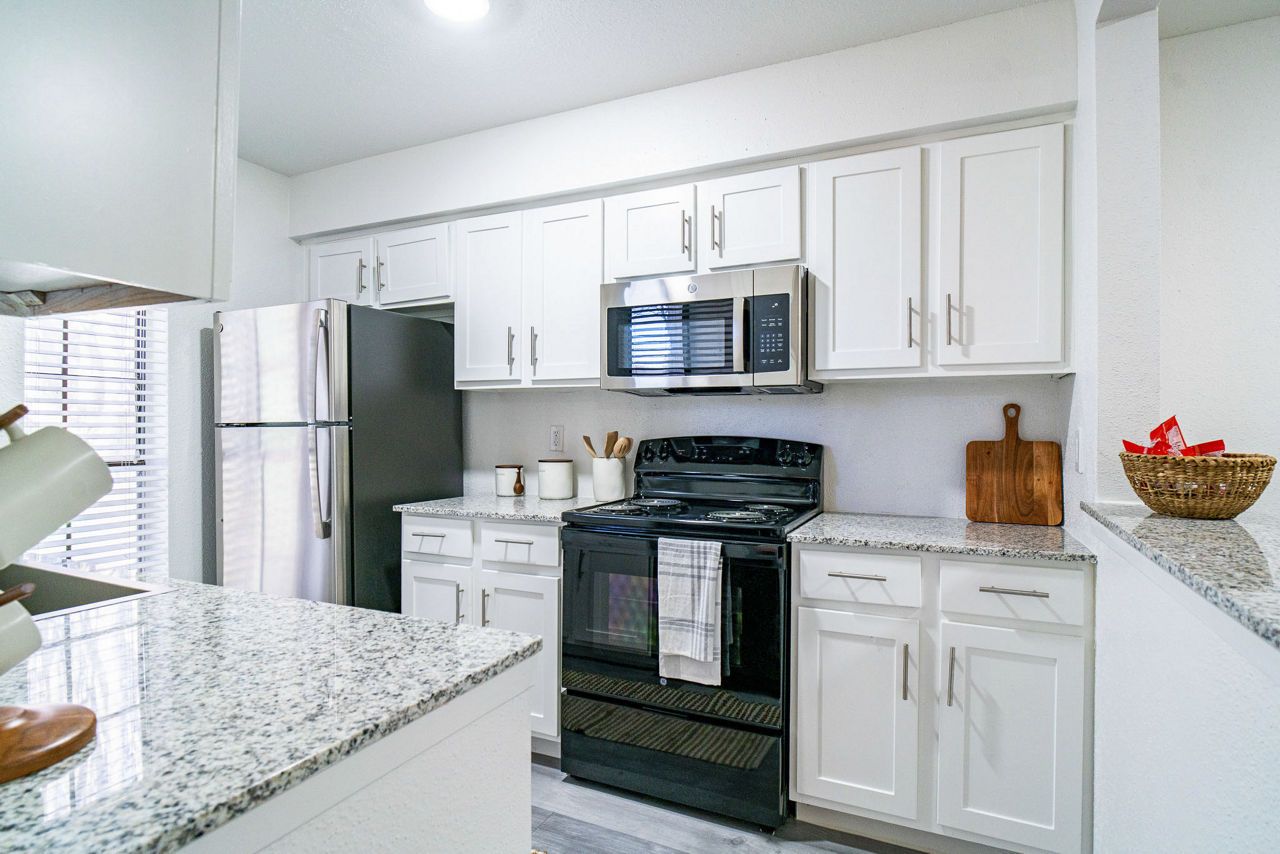 A kitchen with white cabinets, granite countertops, stainless steel appliances, and a black oven in a well-lit space.