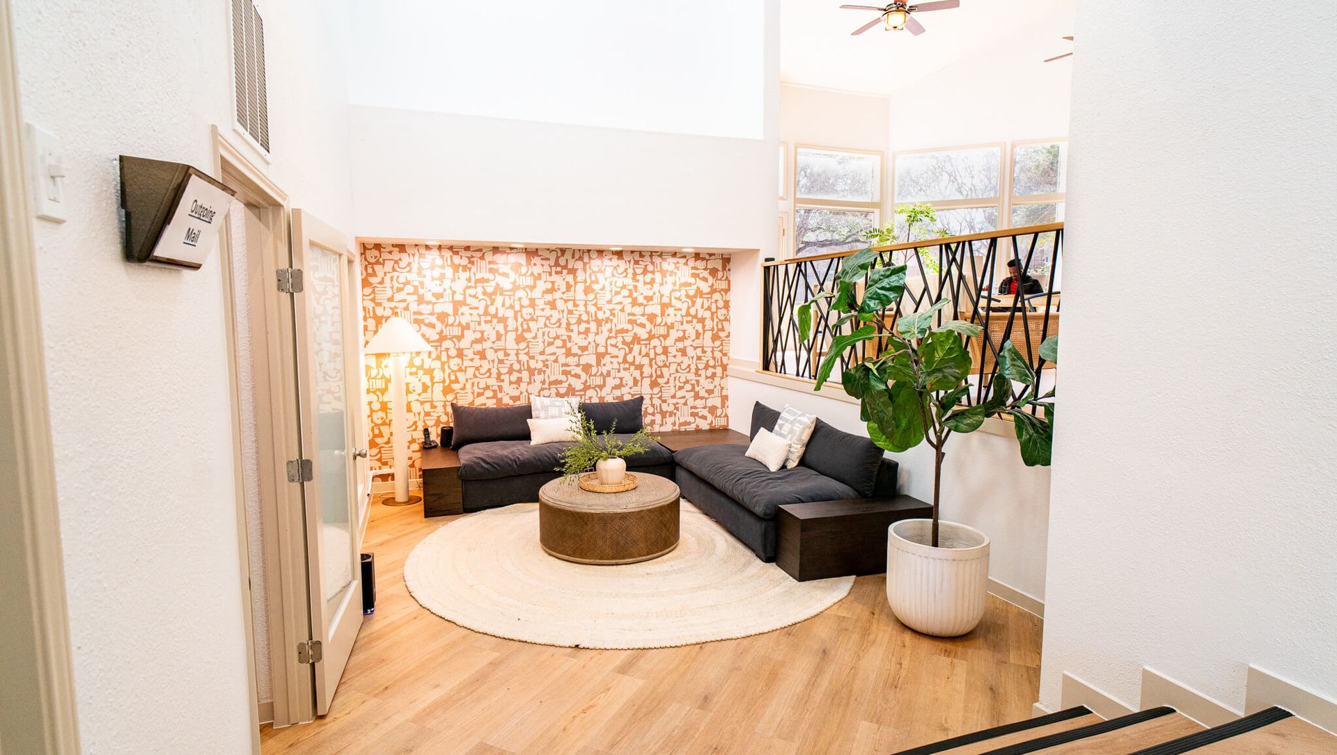 Interior community lounge with sectional sofa, round rug, plants, and a patterned accent wall.
