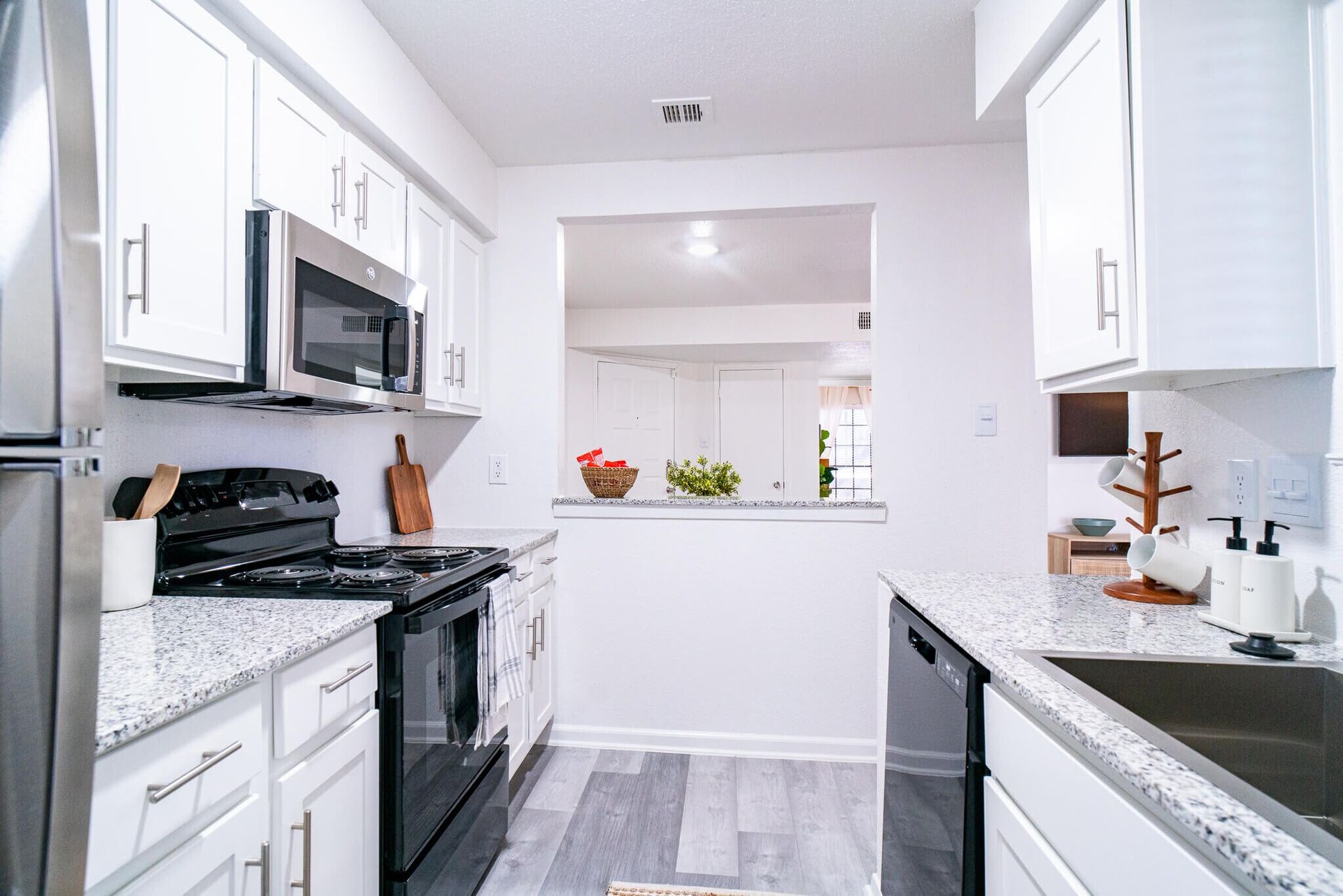A bright kitchen with white cabinets, granite countertops, stainless steel appliances, and wood-look flooring.