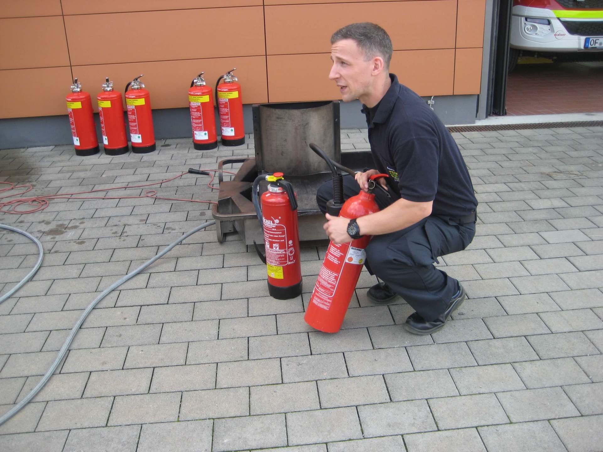 Ein Mann kniet nieder und hält einen roten Feuerlöscher mit einem gelben Aufkleber darauf